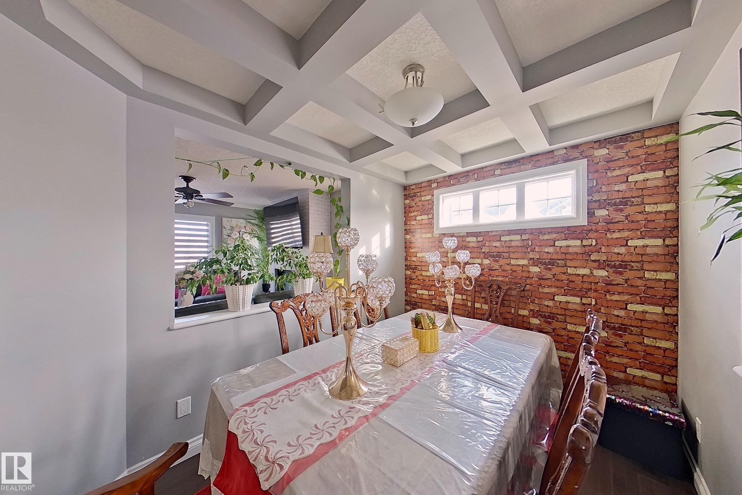 Dining area featuring a coffered ceiling, a decorative brick-style accent wall, and a window providing natural light - 1743 60 Street Sw, Edmonton, AB - Indoor Photo Showing Dining Room