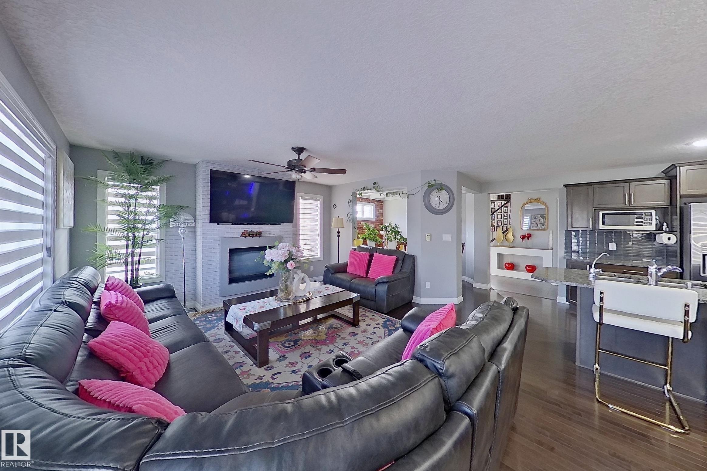 The living area features hard surface flooring, a ceiling fan, and a fireplace with a mounted television - 1743 60 Street Sw, Edmonton, AB - Indoor Photo Showing Living Room With Fireplace