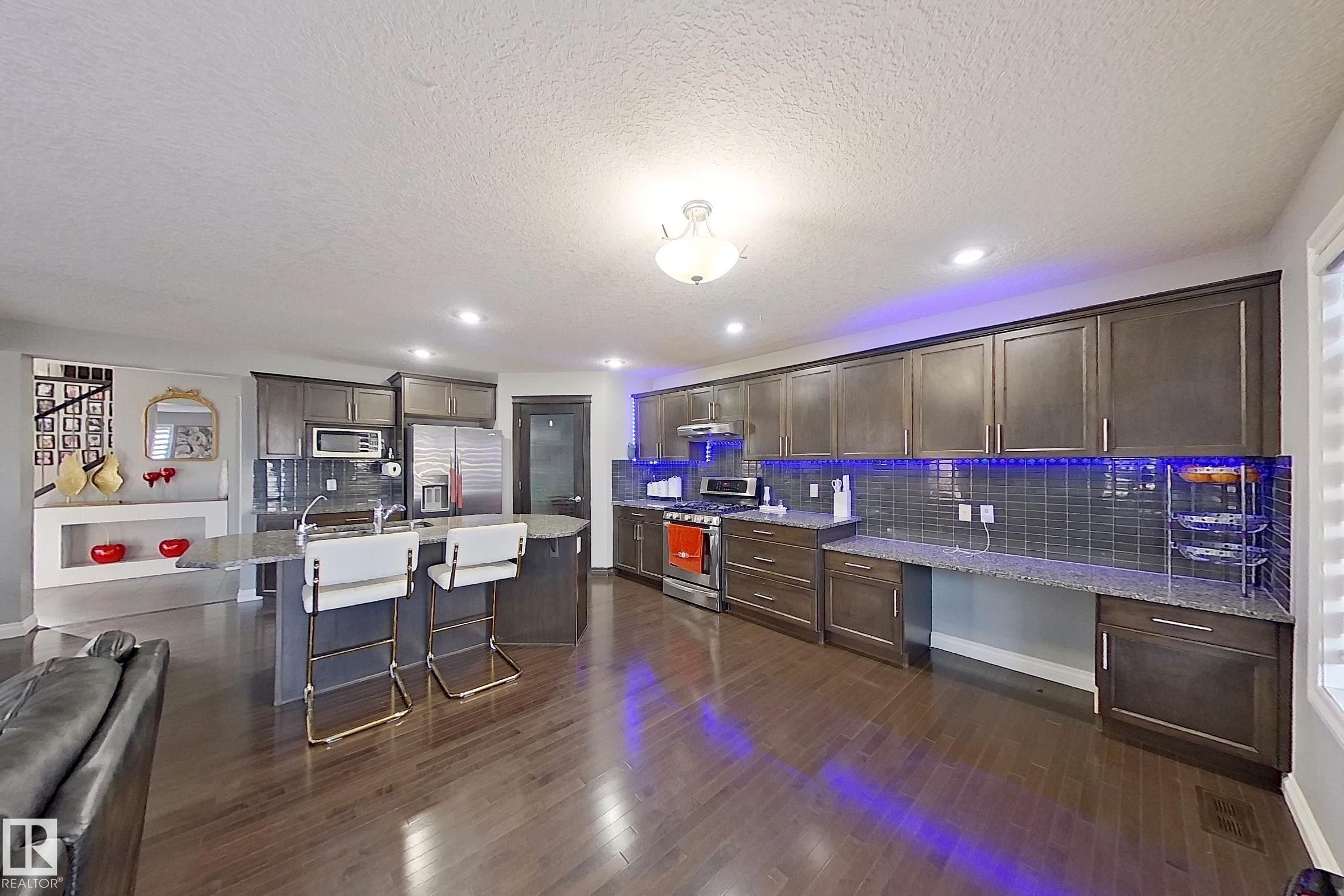 The kitchen features extensive dark wood cabinetry, a tiled backsplash, and stainless steel appliances - 1743 60 Street Sw, Edmonton, AB - Indoor Photo Showing Other Room