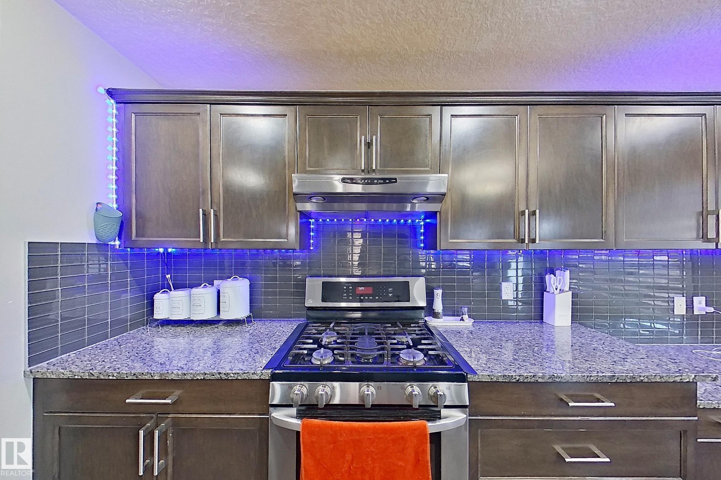 The kitchen features dark wood cabinetry, granite countertops, and a subway tile backsplash - 1743 60 Street Sw, Edmonton, AB - Indoor Photo Showing Kitchen