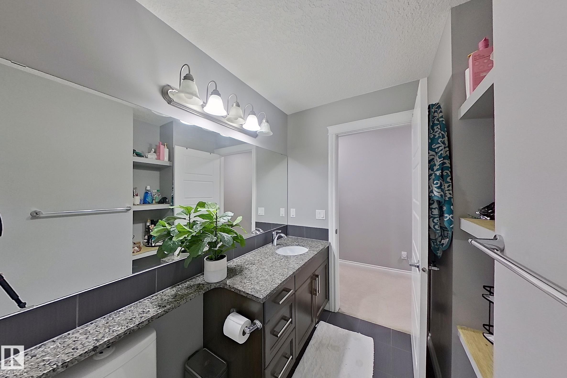 This bathroom features a vanity with a granite countertop, a single basin sink, and ample storage cabinets - 1743 60 Street Sw, Edmonton, AB - Indoor Photo Showing Bathroom