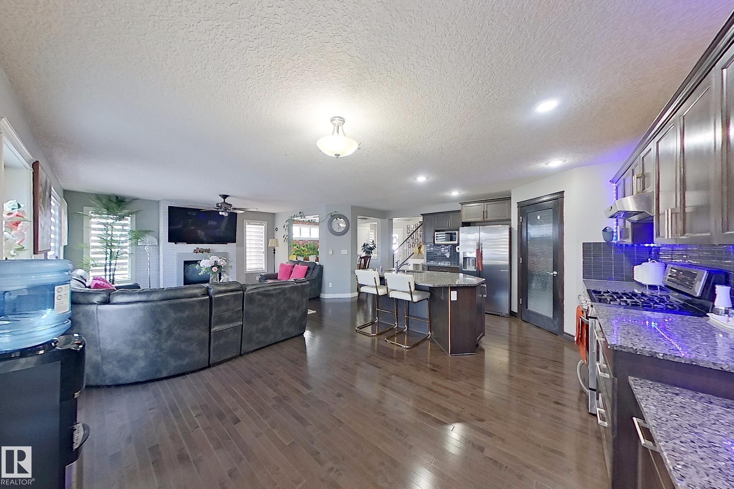 This expansive open-concept living area features hardwood floors, a kitchen with granite countertops, and stainless steel appliances - 1743 60 Street Sw, Edmonton, AB - Indoor
