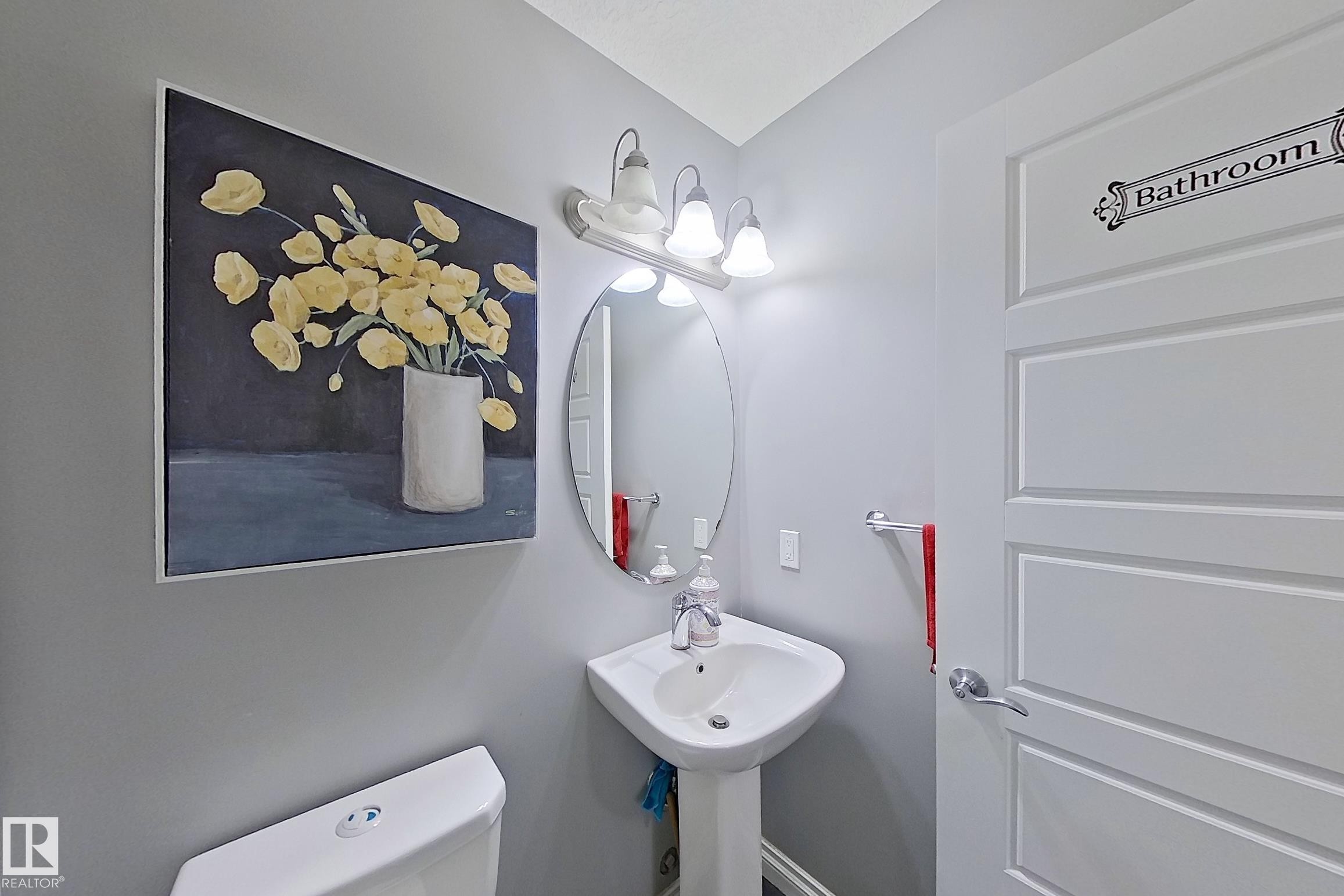 Bathroom featuring a pedestal sink with a mirror and vanity lighting, and a white paneled door - 1743 60 Street Sw, Edmonton, AB - Indoor Photo Showing Bathroom