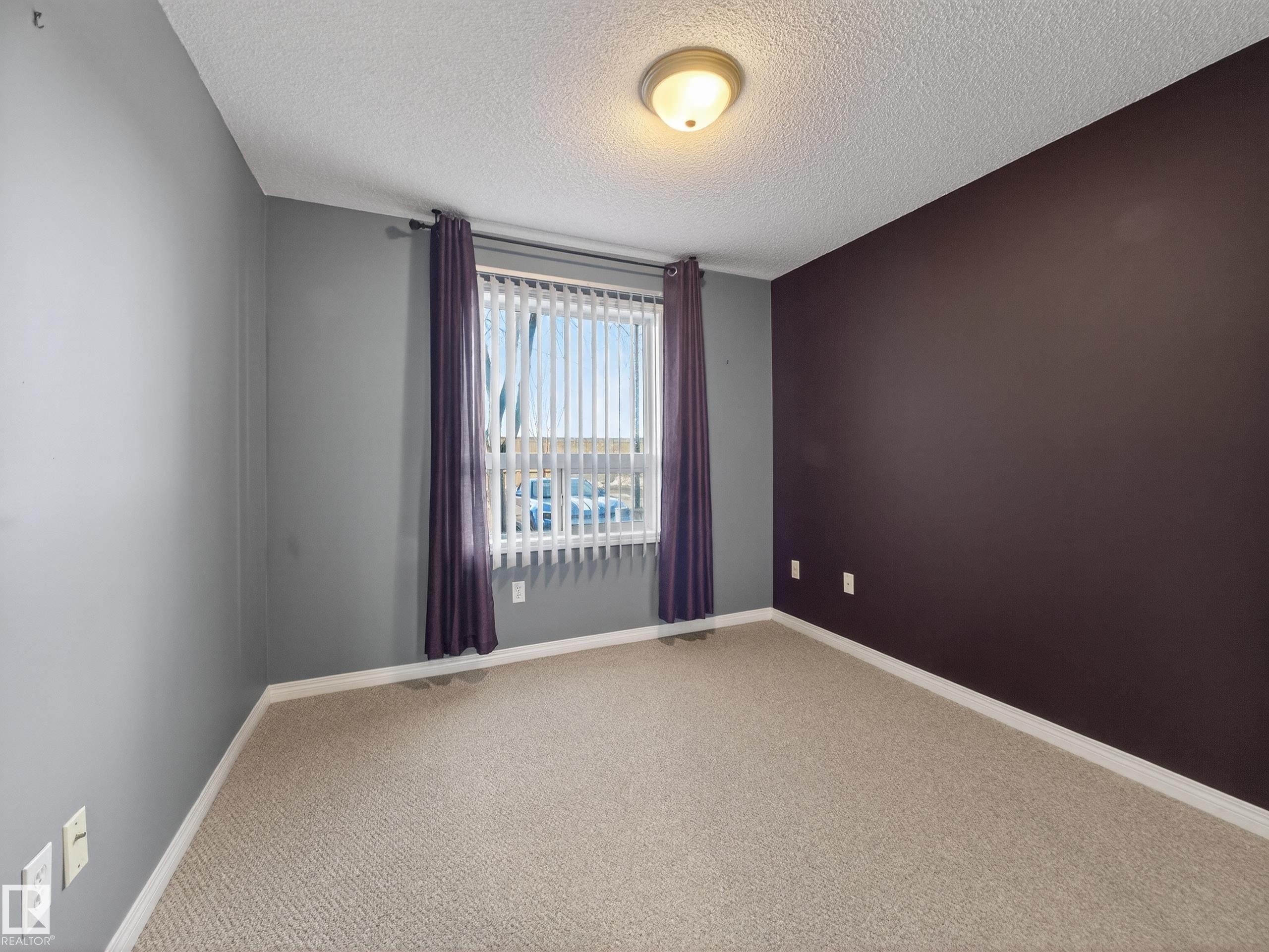 This room features neutral-toned carpeting, a window with vertical blinds and drapes, and a ceiling light fixture - 1111 9363 Simpson Drive, Edmonton, AB - Indoor Photo Showing Other Room