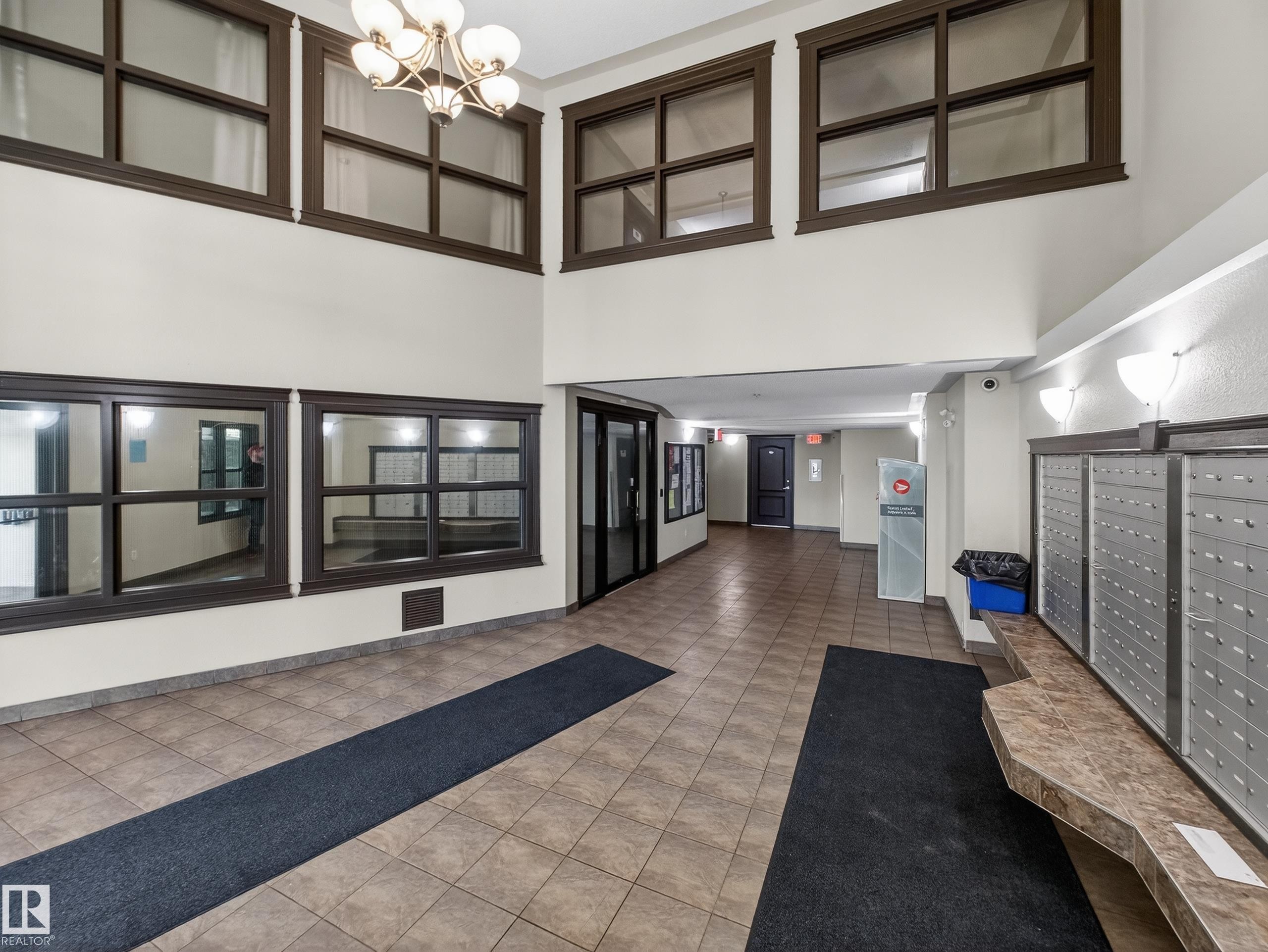 The property features a spacious lobby with tiled flooring, a distinctive chandelier, and large windows - 1111 9363 Simpson Drive, Edmonton, AB - Indoor Photo Showing Other Room