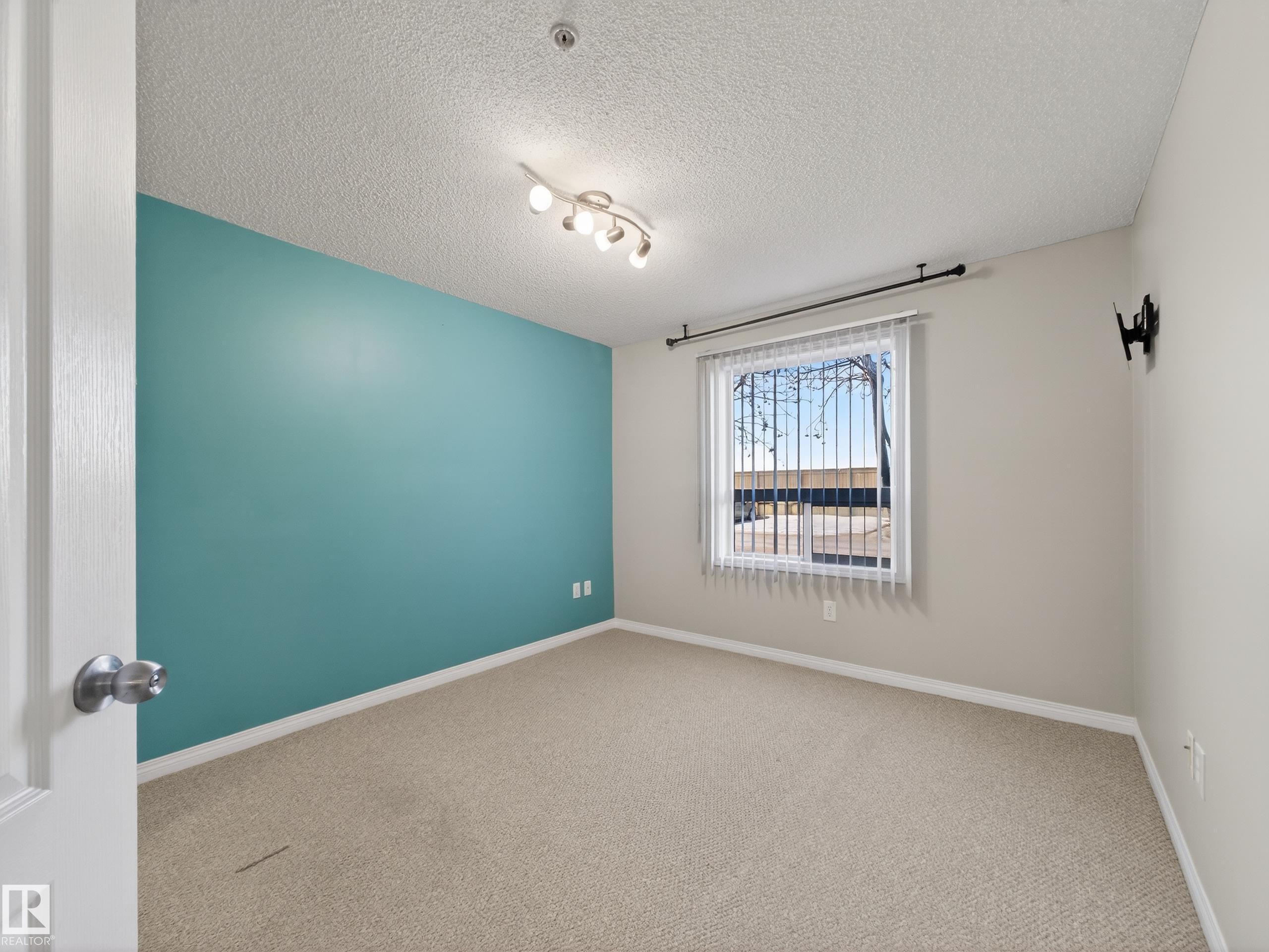 This room features a window with vertical blinds, a ceiling-mounted light fixture, and carpet flooring - 1111 9363 Simpson Drive, Edmonton, AB - Indoor Photo Showing Other Room