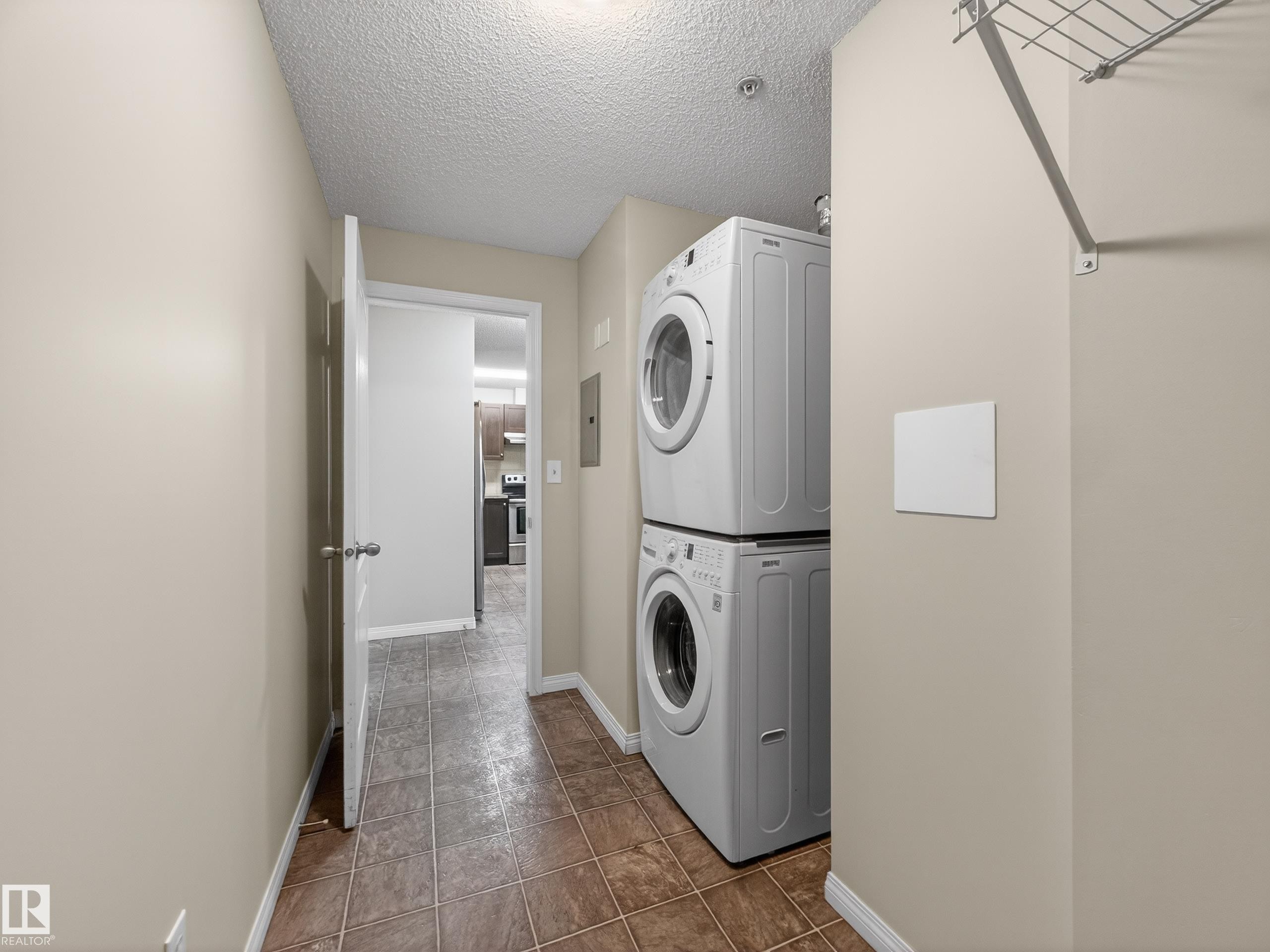 The property features a dedicated laundry area with stacked appliances and a wire shelf for storage - 1111 9363 Simpson Drive, Edmonton, AB - Indoor Photo Showing Laundry Room