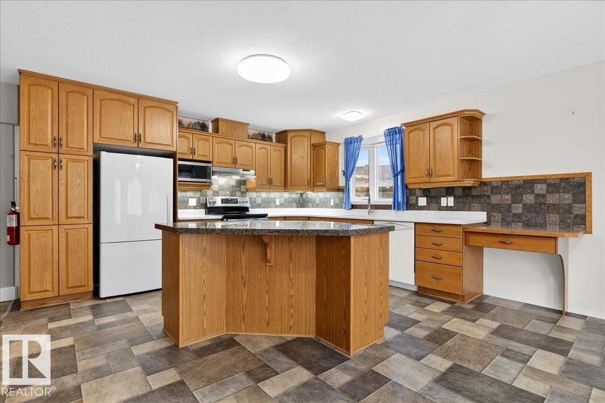 The kitchen features wood cabinetry, a central island with a countertop, and a white refrigerator - 4412 Yeoman Close, Onoway, AB - Indoor Photo Showing Kitchen