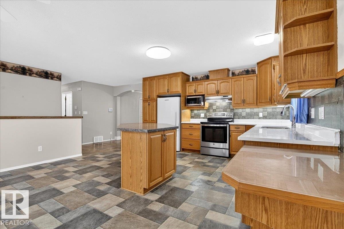 Kitchen featuring wood cabinetry, stainless steel appliances, a center island with a stone countertop, and tile flooring - 4412 Yeoman Close, Onoway, AB - Indoor Photo Showing Kitchen
