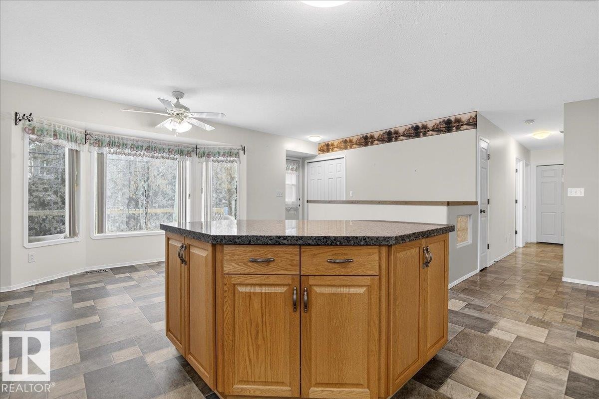 Kitchen featuring a central island with a granite countertop and wood cabinetry, bay windows, and tiled flooring - 4412 Yeoman Close, Onoway, AB - Indoor Photo Showing Kitchen