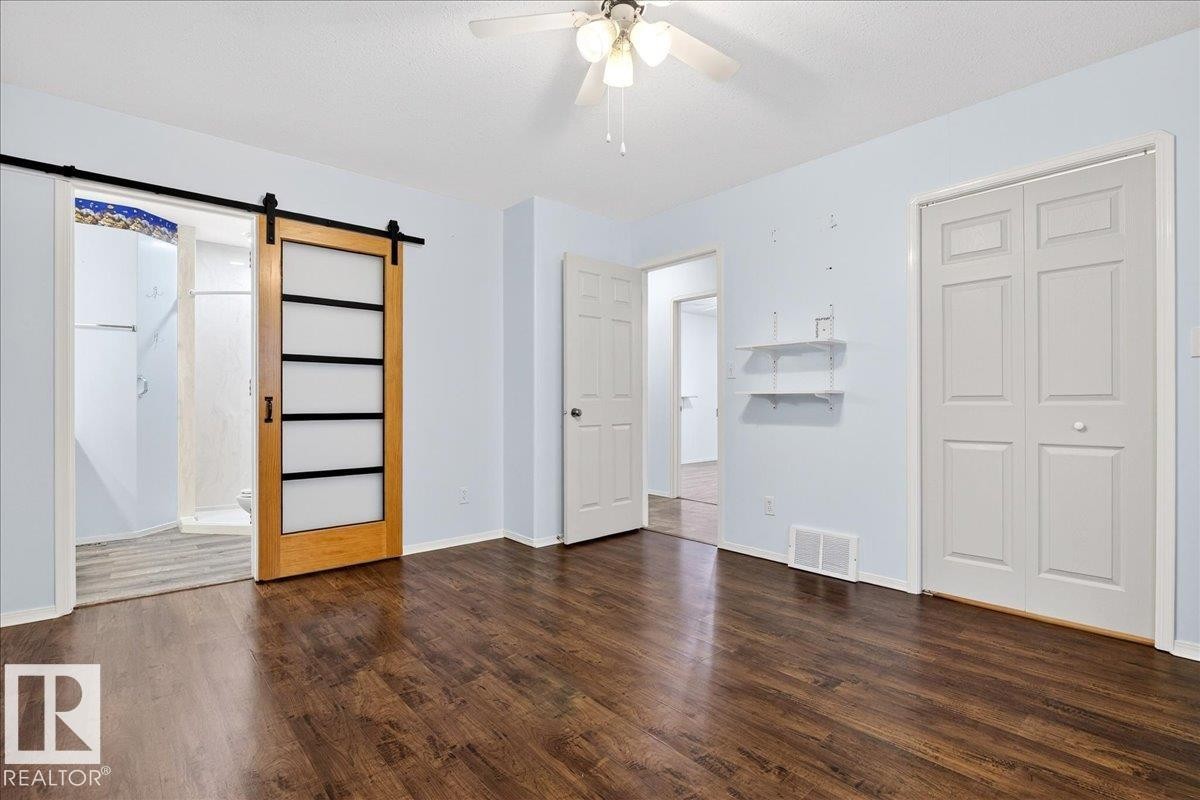 This room features dark wood flooring, a ceiling fan with integrated lighting, and a barn door entry to a separate area - 4412 Yeoman Close, Onoway, AB - Indoor Photo Showing Other Room