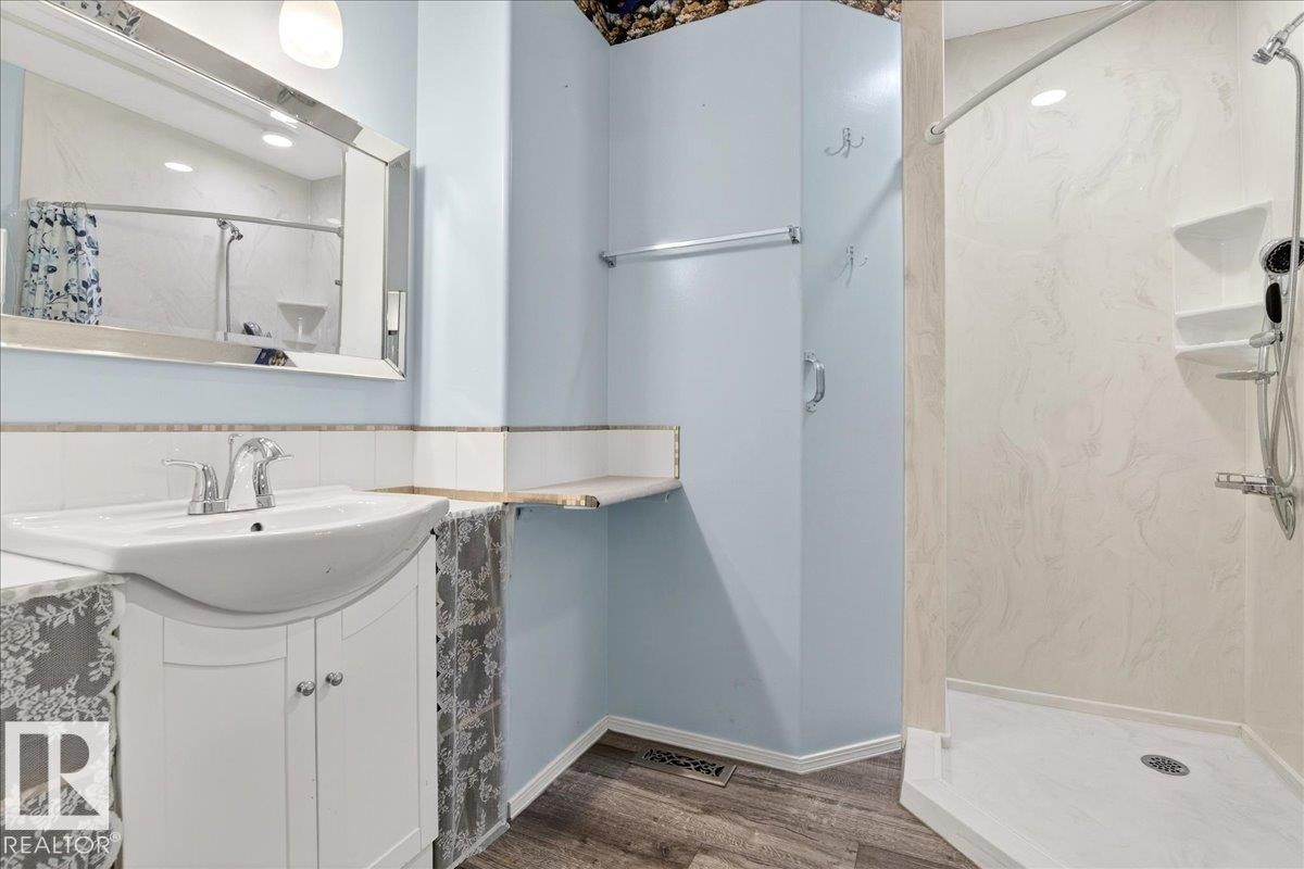 This bathroom features a vanity with a white sink and chrome faucet, a wall-mounted mirror, and a walk-in shower with shelving - 4412 Yeoman Close, Onoway, AB - Indoor Photo Showing Bathroom