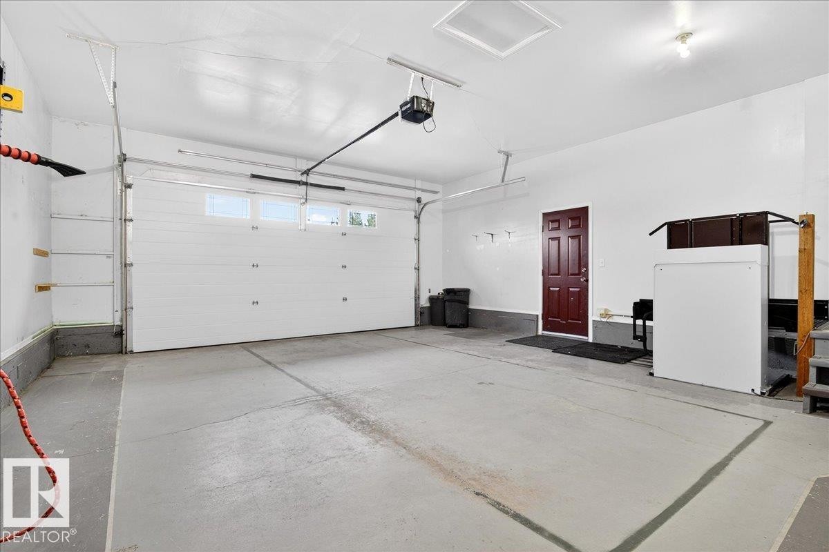 Attached garage featuring a white overhead door with windows, concrete flooring, and a dark wood interior door - 4412 Yeoman Close, Onoway, AB - Indoor Photo Showing Garage