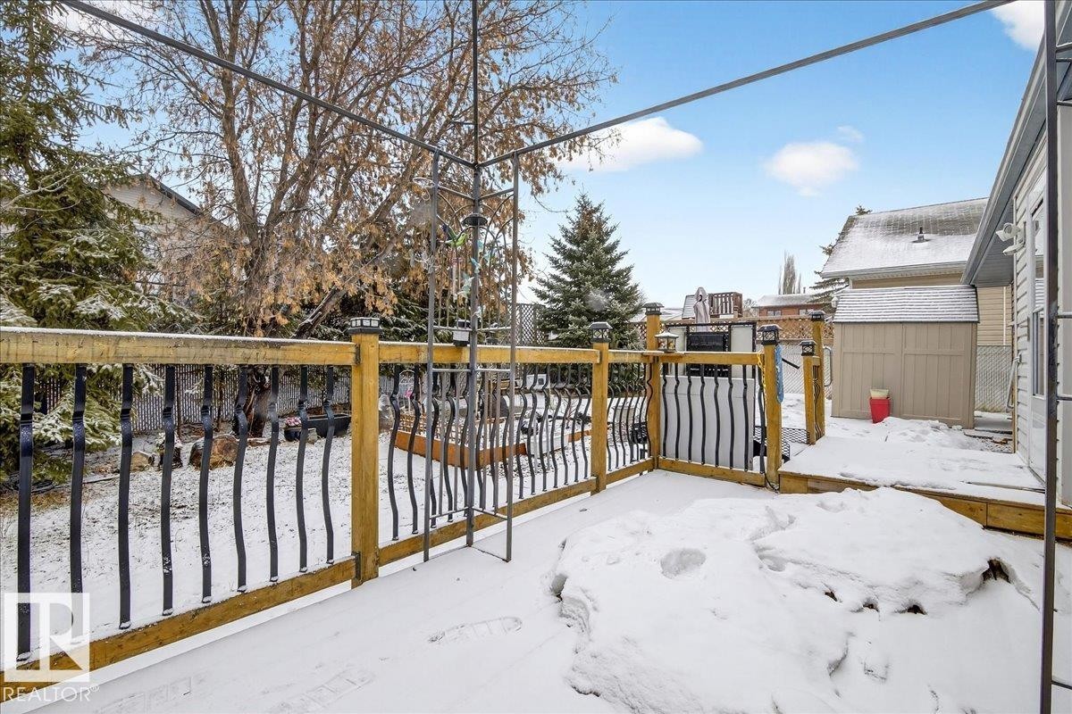 The property features a wood deck with a metal railing, overlooking a fenced yard with mature trees - 4412 Yeoman Close, Onoway, AB - Outdoor