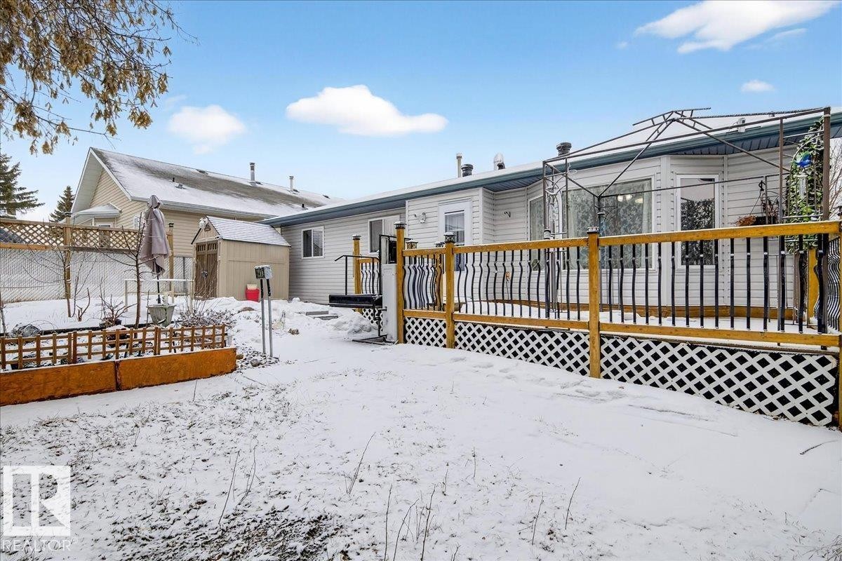 The property features a spacious deck with a wooden railing and lattice skirting, overlooking a snowy yard - 4412 Yeoman Close, Onoway, AB - Outdoor With Deck Patio Veranda