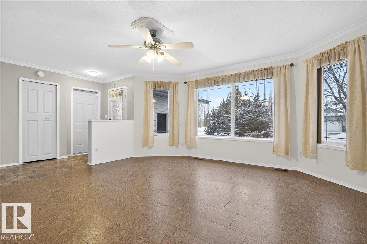 This area features a ceiling fan, bay windows with drapes, and durable flooring, with white doors and trim visible - 4412 Yeoman Close, Onoway, AB - Indoor Photo Showing Other Room