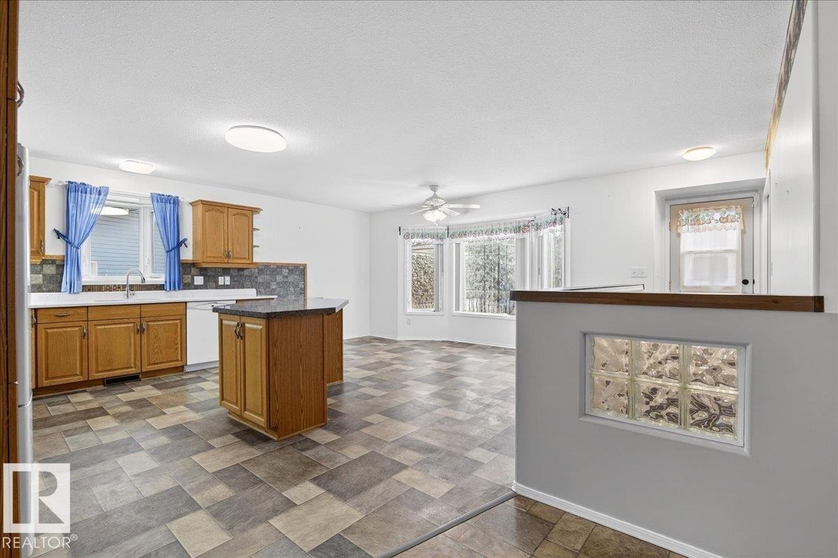The kitchen features wood cabinetry, a central island with a dark countertop, and tiled flooring - 4412 Yeoman Close, Onoway, AB - Indoor Photo Showing Kitchen