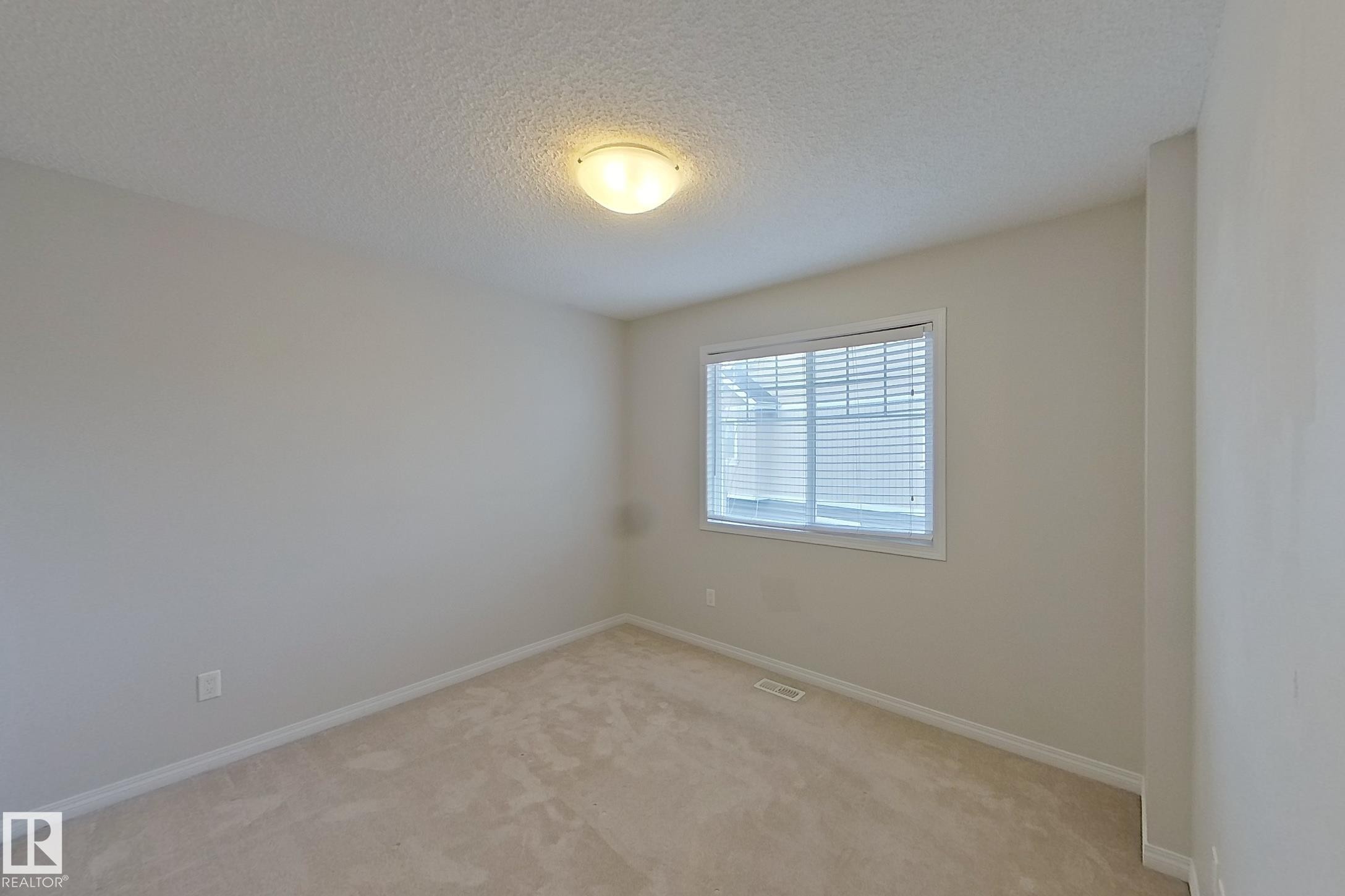 This room features light-toned carpeting, a window with blinds, and an overhead flush mount light fixture - 87 4050 Savaryn Drive, Edmonton, AB - Indoor Photo Showing Other Room
