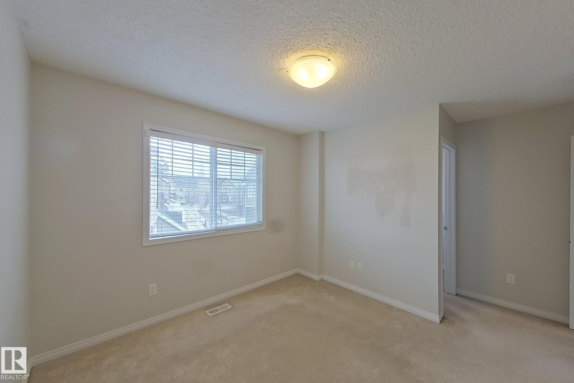 This room features neutral-toned carpet flooring, a window with horizontal blinds, and a ceiling-mounted light fixture - 87 4050 Savaryn Drive, Edmonton, AB - Indoor Photo Showing Other Room