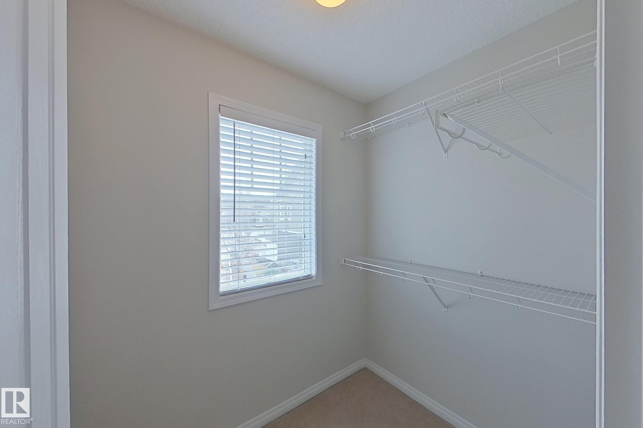 This space features a window with blinds, carpeted flooring, and white wire shelving - 87 4050 Savaryn Drive, Edmonton, AB - Indoor With Storage