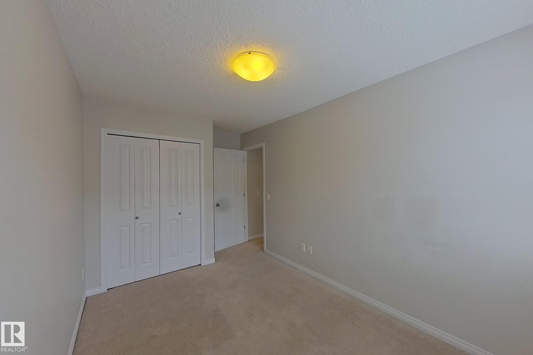 This room features neutral-toned carpet flooring, light-colored walls, and a ceiling-mounted light fixture - 87 4050 Savaryn Drive, Edmonton, AB - Indoor