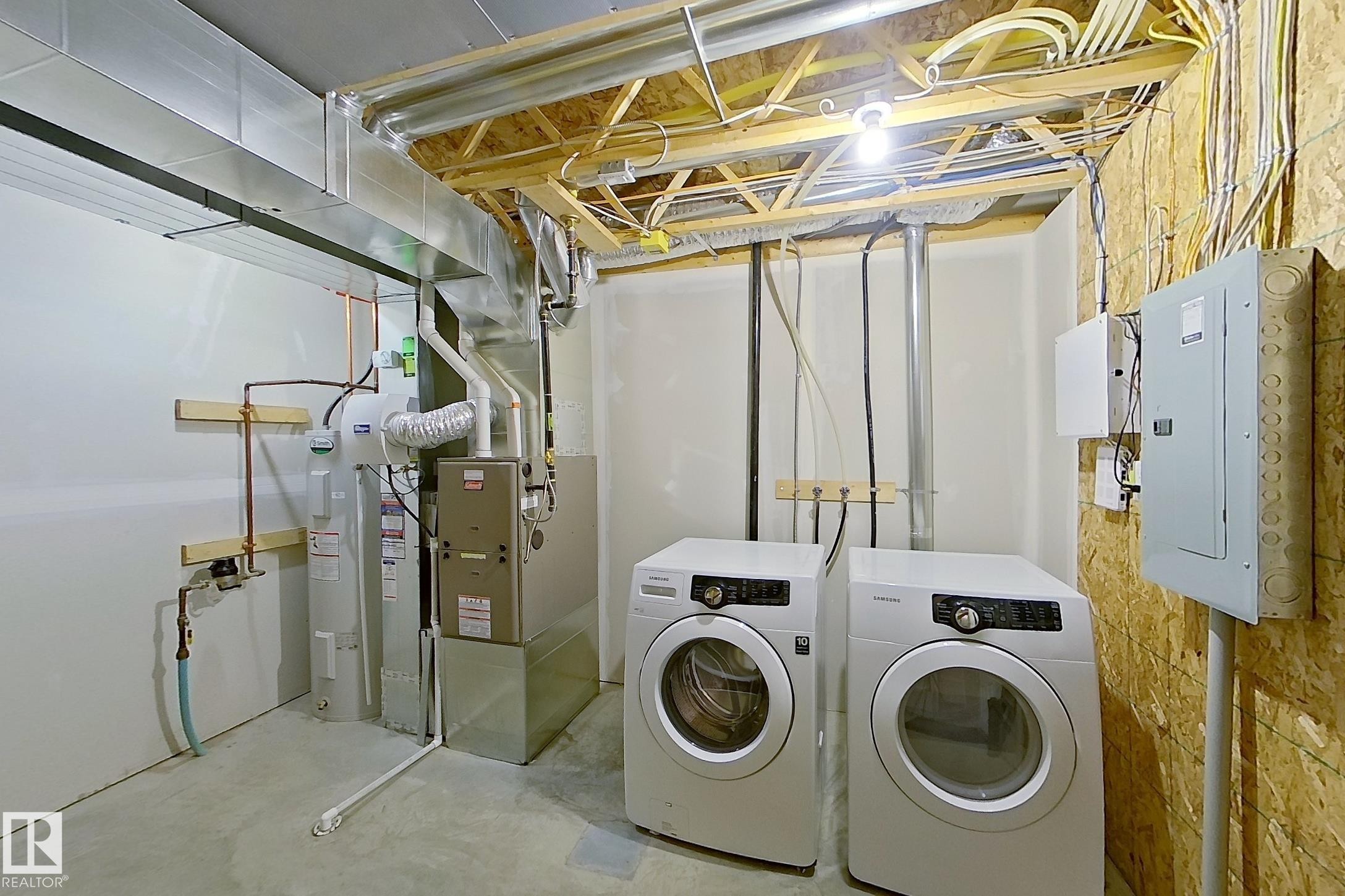 This utility area features a clothes washer and dryer, a water heater, and a furnace, all set on a concrete floor - 87 4050 Savaryn Drive, Edmonton, AB - Indoor Photo Showing Laundry Room