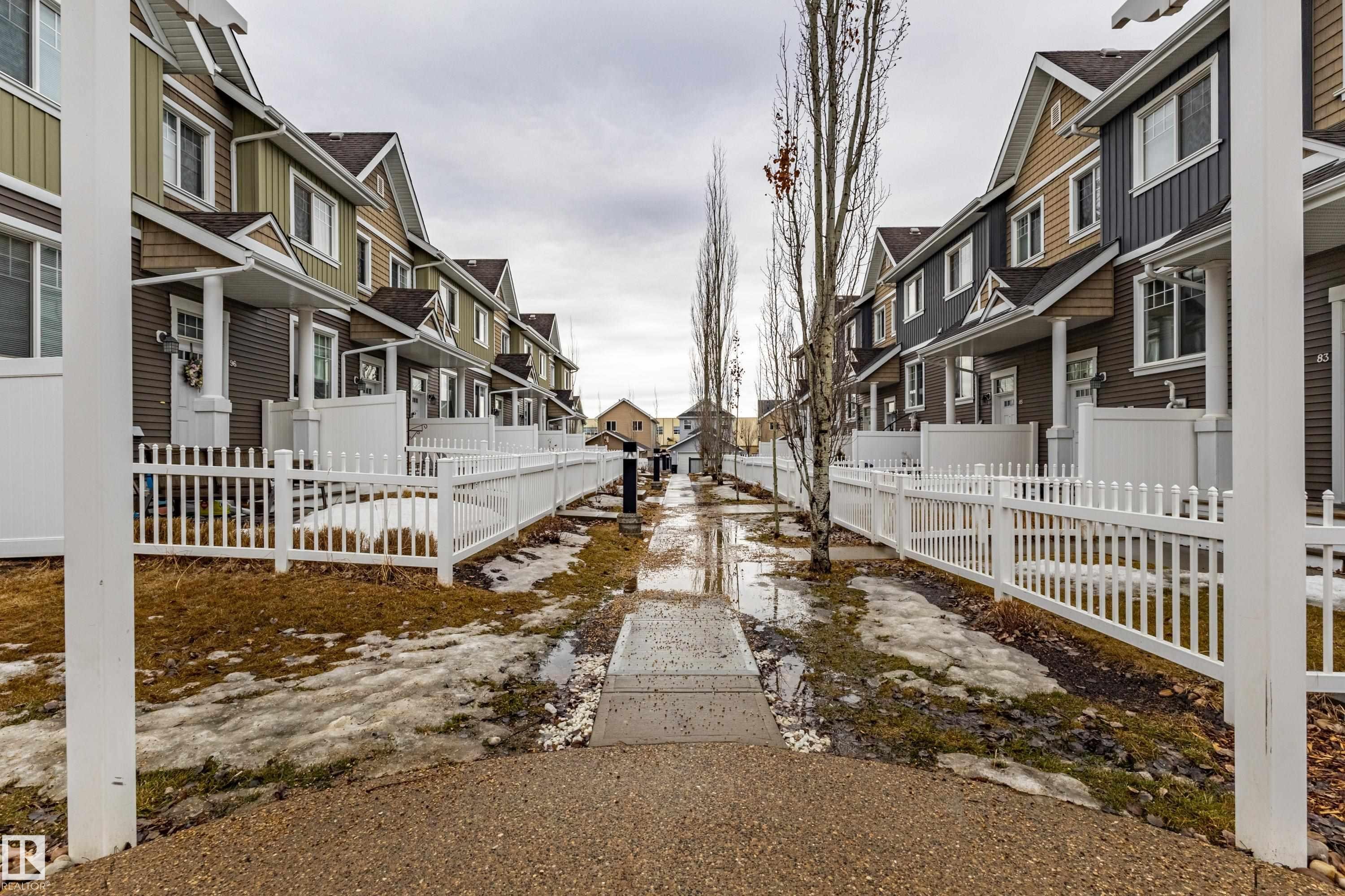 The property is part of a row of residences featuring varied exterior siding colors and white picket fences - 87 4050 Savaryn Drive, Edmonton, AB - Outdoor With Deck Patio Veranda
