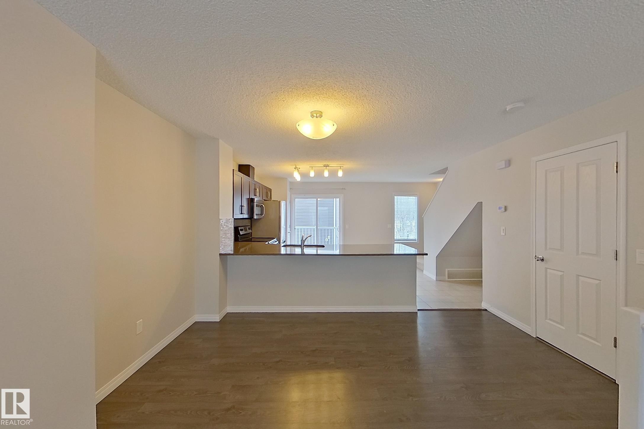 Open concept living area featuring dark flooring, light-colored walls, and a kitchen with dark cabinetry, stainless steel appliances, and a breakfast bar - 87 4050 Savaryn Drive, Edmonton, AB - Indoor Photo Showing Other Room