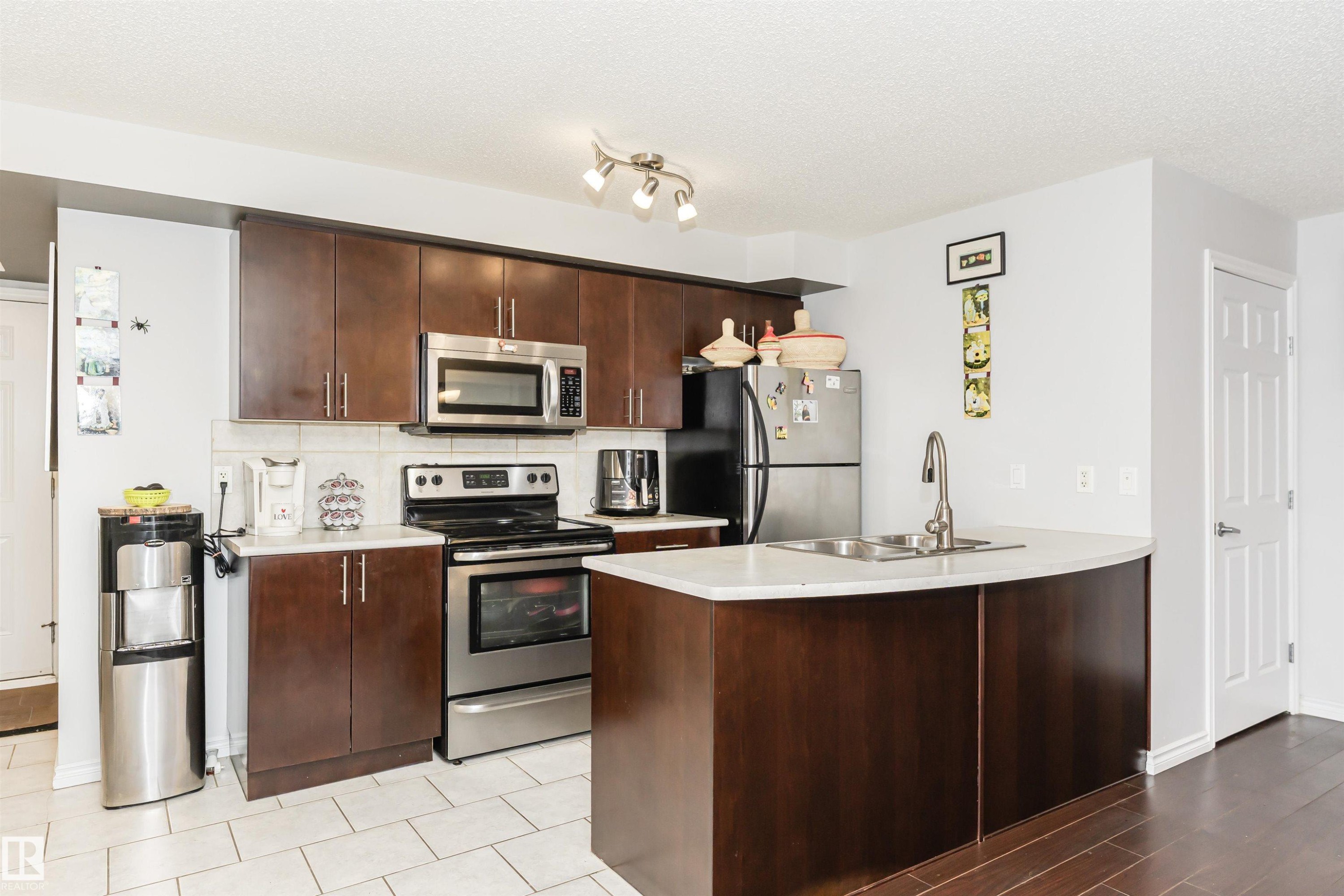 The kitchen features dark wood cabinetry, stainless steel appliances, and a kitchen island with a double sink - 107 10118 106 Avenue, Edmonton, AB - Indoor Photo Showing Kitchen