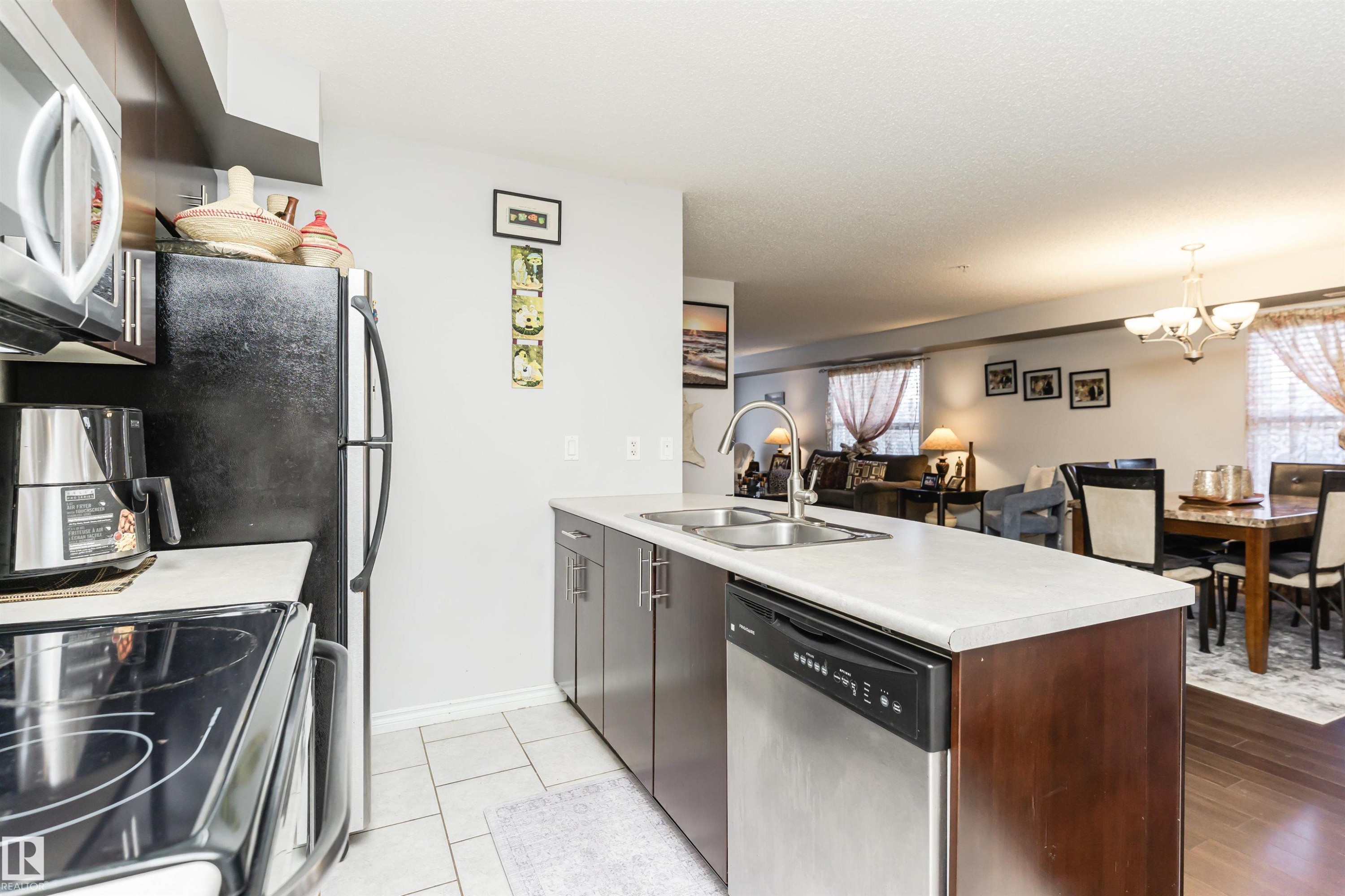 The kitchen features a stainless steel refrigerator, microwave, and dishwasher, with a double basin sink and dark wood cabinetry - 107 10118 106 Avenue, Edmonton, AB - Indoor Photo Showing Kitchen With Double Sink
