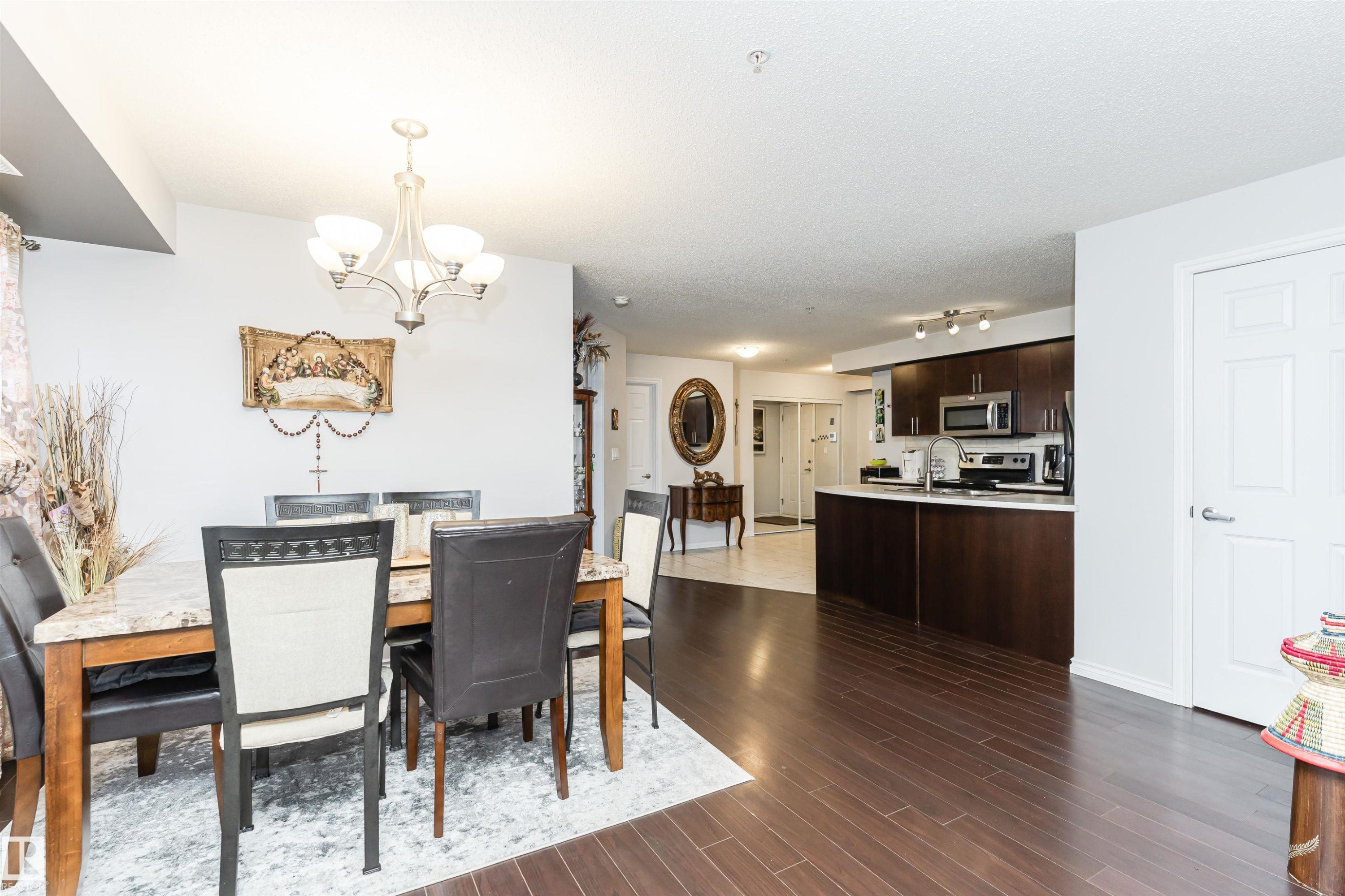 Open concept living space featuring dark hardwood flooring, a dining area with a chandelier, and a kitchen with dark cabinetry and stainless steel appliances - 107 10118 106 Avenue, Edmonton, AB - Indoor Photo Showing Dining Room