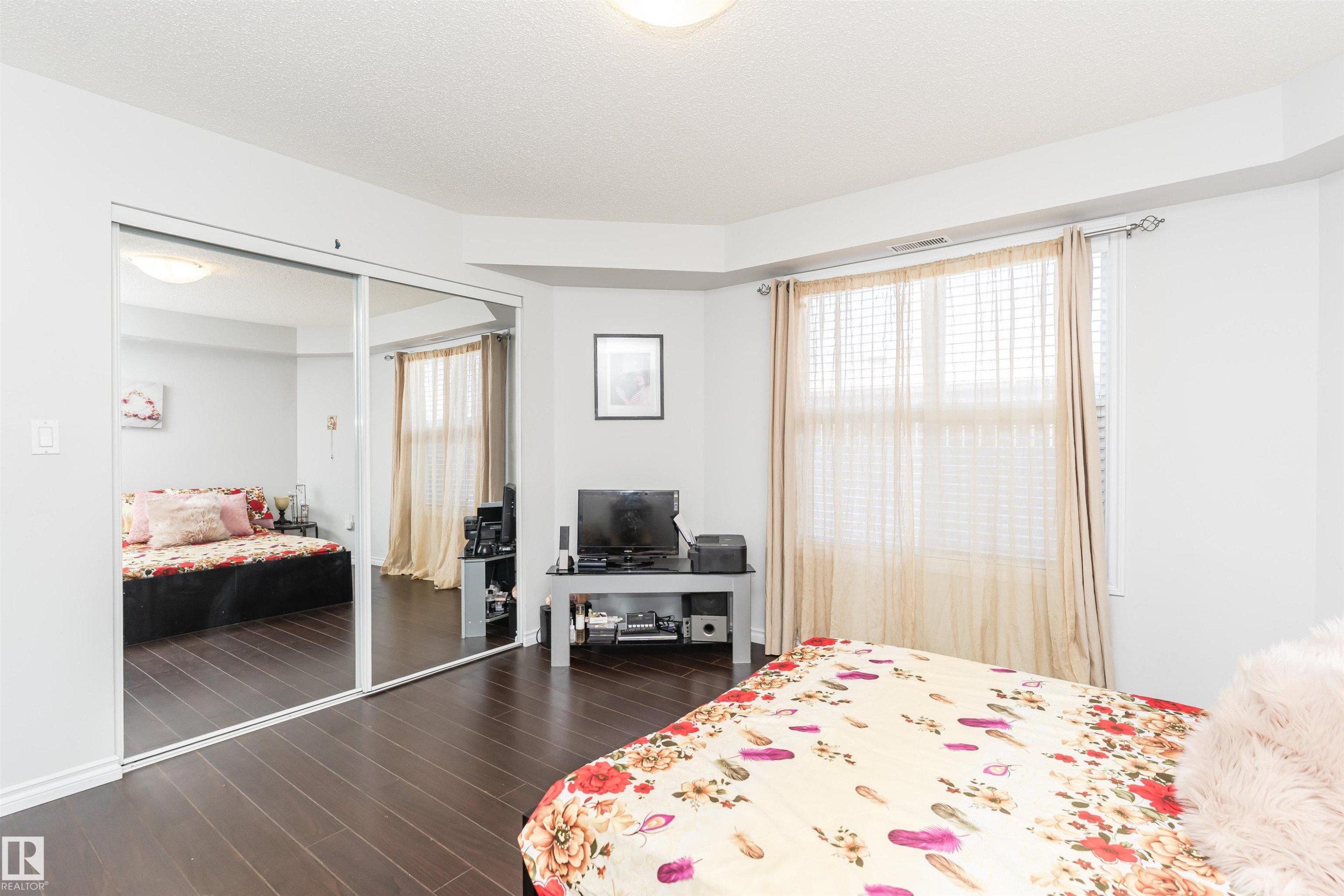 This room features dark wood flooring, a window with blinds and curtains, and a large closet with mirrored sliding doors - 107 10118 106 Avenue, Edmonton, AB - Indoor Photo Showing Bedroom
