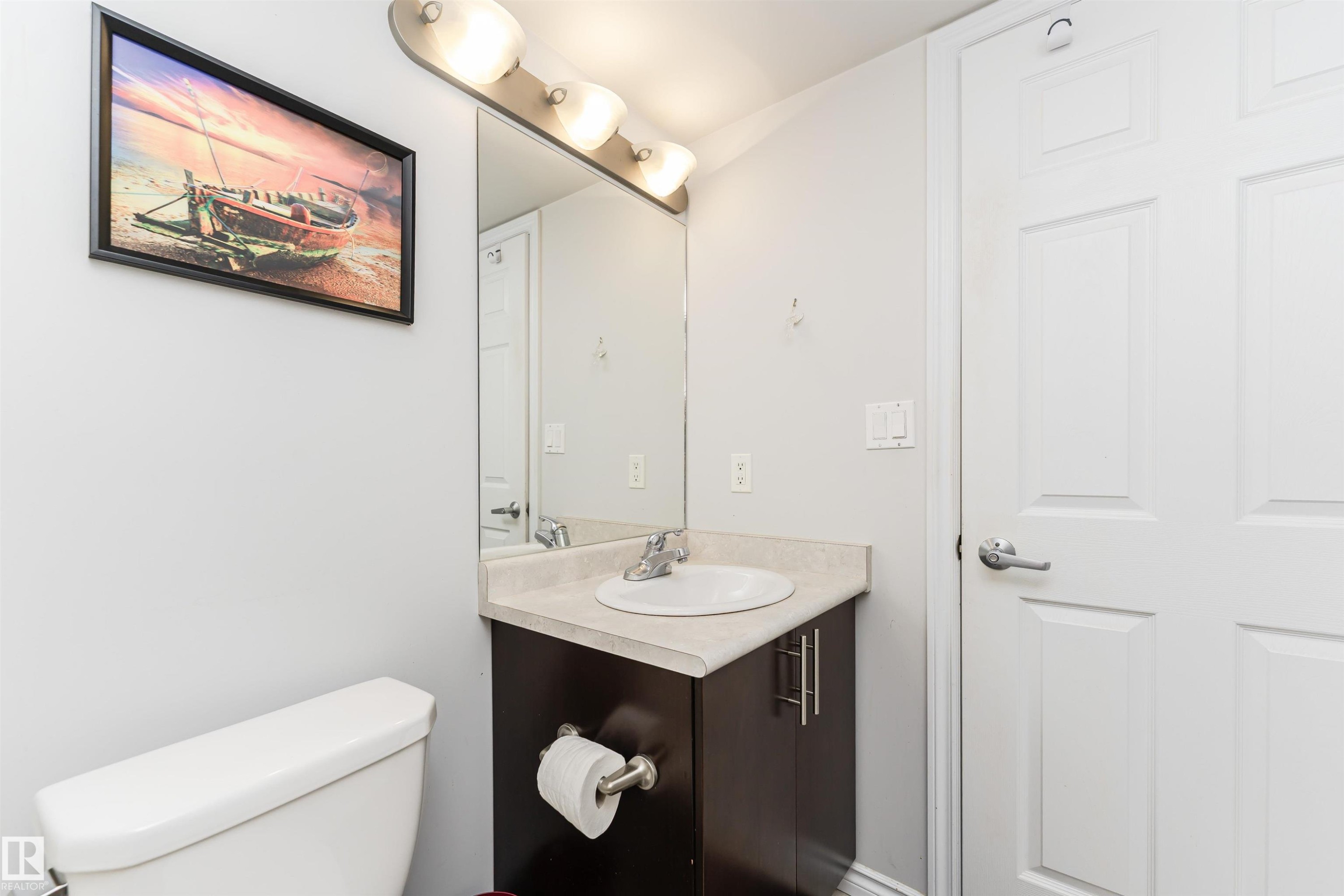 A well-appointed bathroom featuring a white toilet, a vanity with an integrated sink, and a mirror with overhead lighting - 107 10118 106 Avenue, Edmonton, AB - Indoor Photo Showing Bathroom