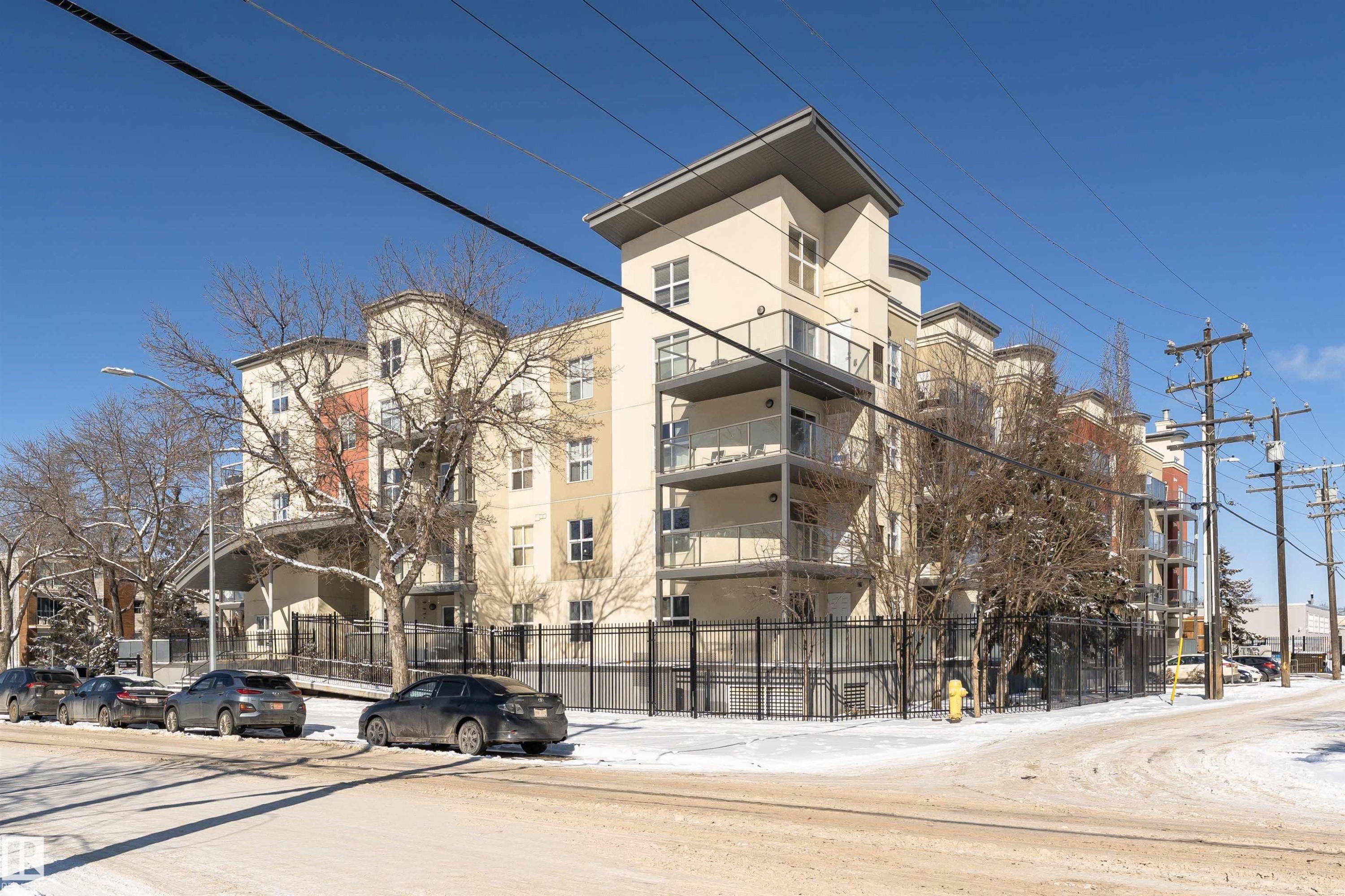 The property features a multi-story building with a light-colored facade, private balconies, and a surrounding security fence - 107 10118 106 Avenue, Edmonton, AB - Outdoor