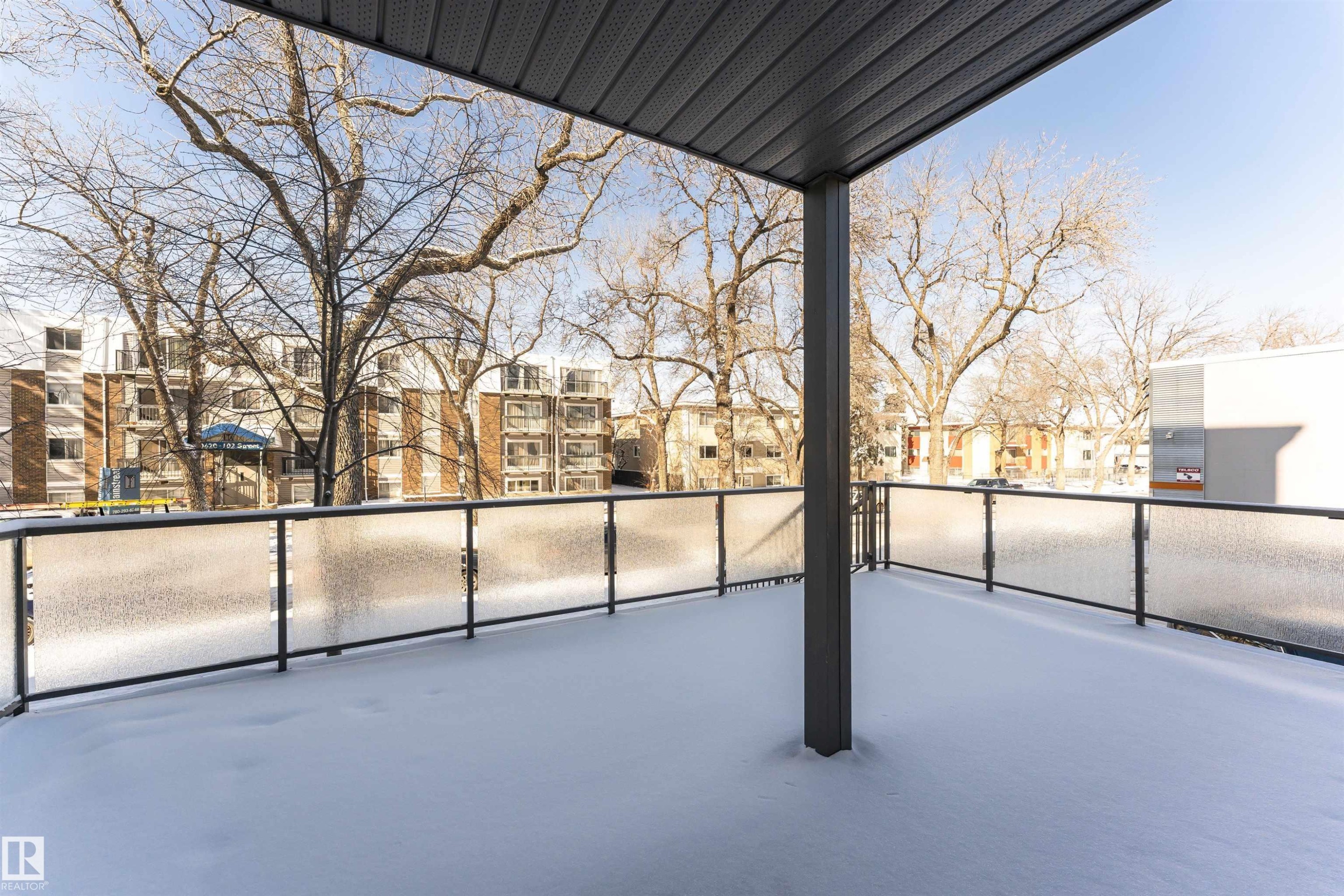 The property features an outdoor balcony with a frosted glass and black metal railing, and a dark grey overhead covering - 107 10118 106 Avenue, Edmonton, AB - Outdoor