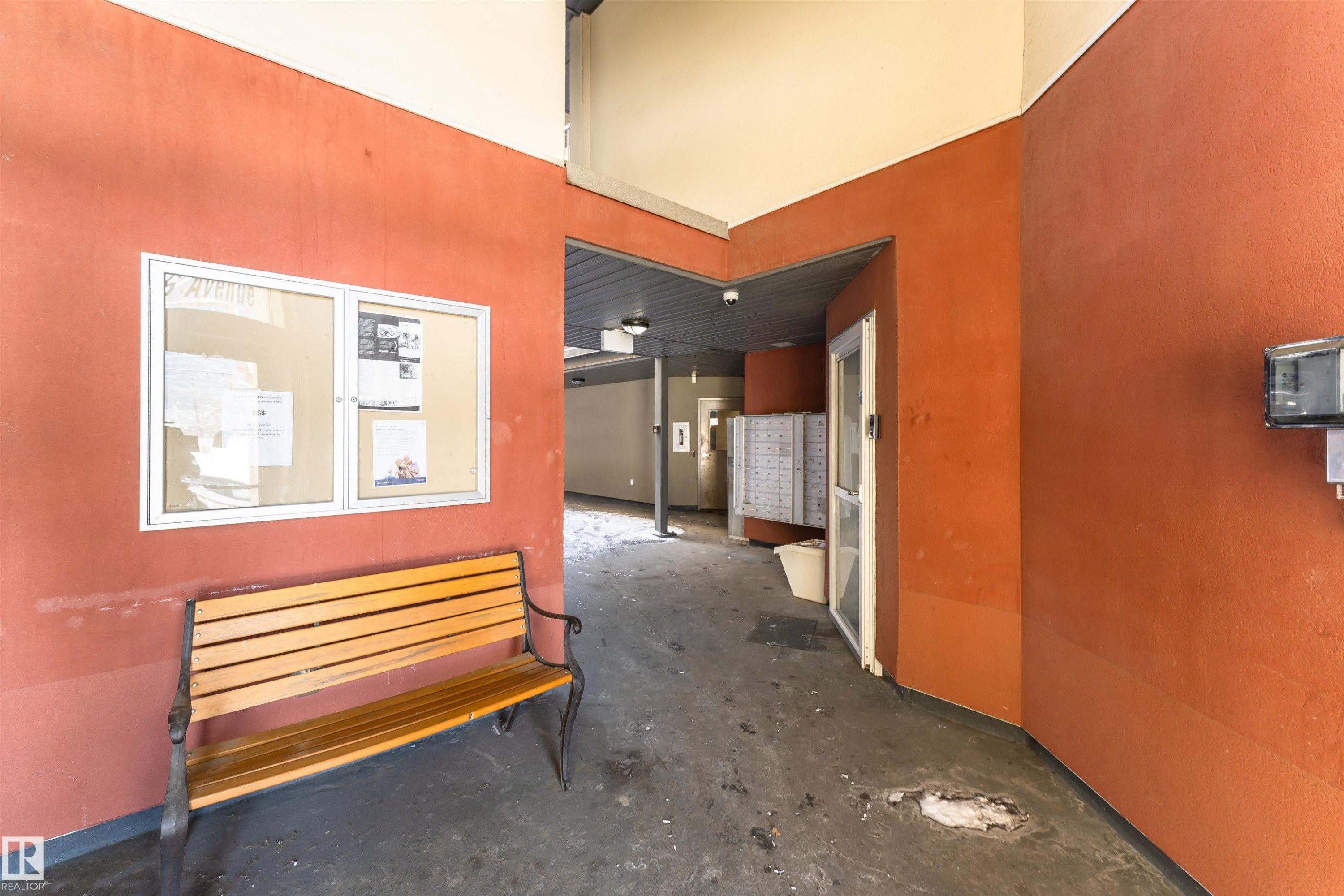 The property features a community area with a wooden bench, a wall-mounted bulletin board, and a bank of mailboxes - 107 10118 106 Avenue, Edmonton, AB - Indoor Photo Showing Other Room