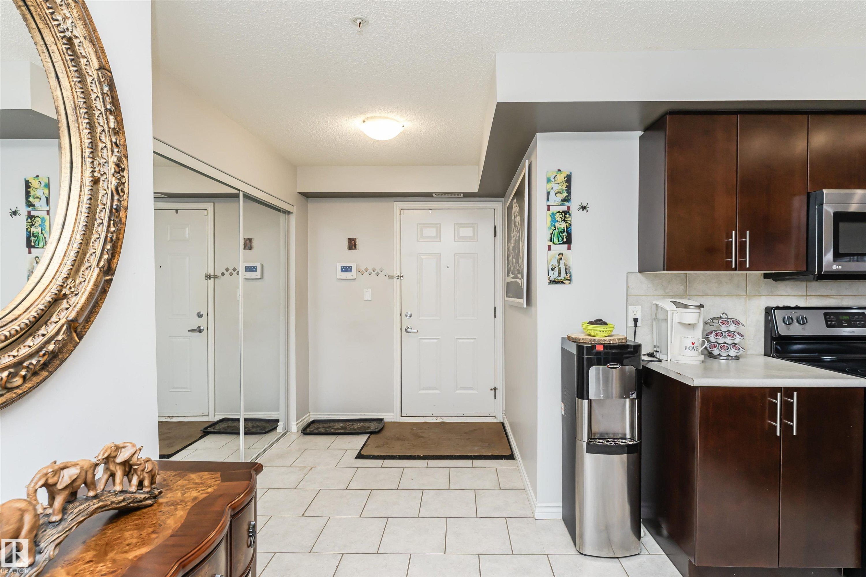 The property features a kitchen with dark wood cabinetry, a tiled backsplash, and stainless steel appliances - 107 10118 106 Avenue, Edmonton, AB - Indoor Photo Showing Kitchen