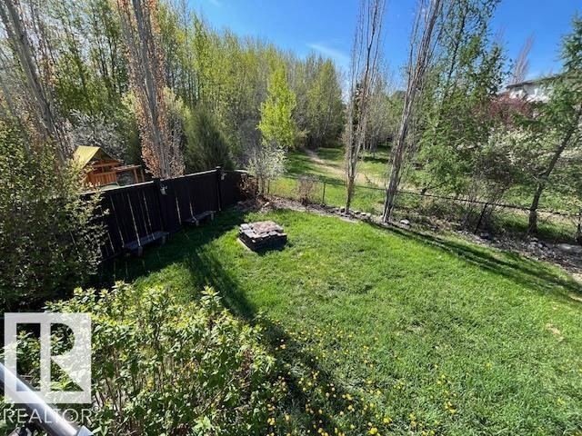 Manicured lawn area featuring a central fire pit, dark wood fencing, and a separate play structure - 21917 95A Avenue, Edmonton, AB - Outdoor