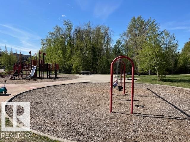 Outdoor play area featuring a red and brown playground structure, a red swing set, wood chip surfacing, paved pathways, and surrounding mature trees - 21917 95A Avenue, Edmonton, AB - Outdoor