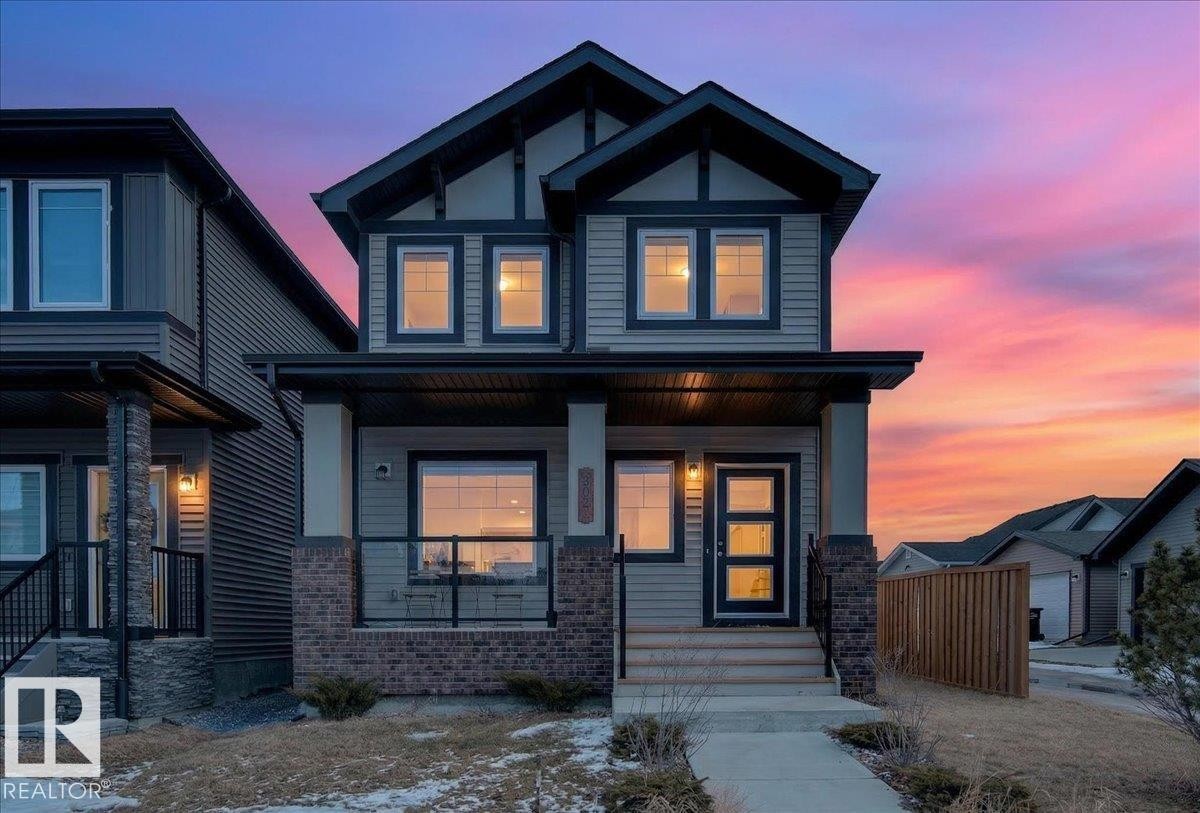 The property features a two-story exterior with light-colored siding, dark trim, and a prominent front entrance - 203 Cavanagh Common, Edmonton, AB - Outdoor With Facade