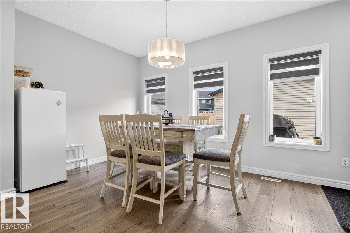 The dining area features light hardwood flooring, light grey walls, and a modern drum pendant light fixture - 203 Cavanagh Common, Edmonton, AB - Indoor Photo Showing Dining Room
