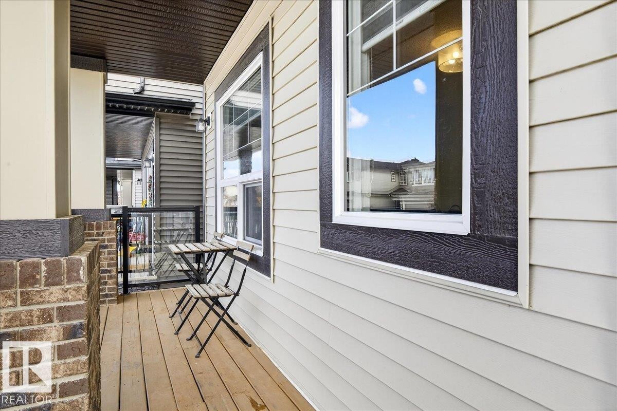 The property features a balcony with wood decking, brick accents, and light-colored siding - 203 Cavanagh Common, Edmonton, AB - Outdoor With Deck Patio Veranda With Exterior