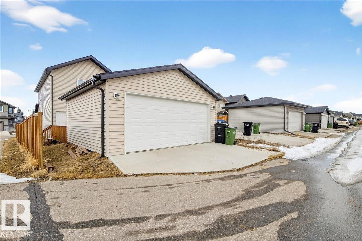 The property features a detached garage with a white garage door, concrete driveway, and light-colored siding - 203 Cavanagh Common, Edmonton, AB - Outdoor