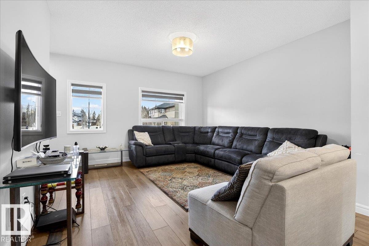 Living area with hardwood flooring, light grey walls, and two windows providing natural light - 203 Cavanagh Common, Edmonton, AB - Indoor Photo Showing Living Room