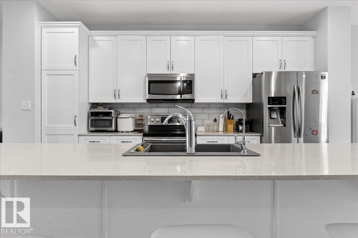 Kitchen featuring white cabinetry, a stainless steel refrigerator, and a double basin sink with a chrome faucet - 203 Cavanagh Common, Edmonton, AB - Indoor Photo Showing Kitchen With Double Sink With Upgraded Kitchen