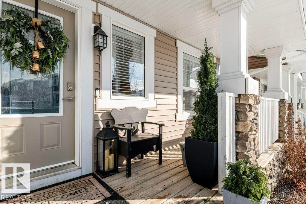 The property features a welcoming porch with a wood deck, stone-accented pillars, and a decorative outdoor lantern - 16720 15 Avenue, Edmonton, AB - Outdoor With Deck Patio Veranda With Exterior