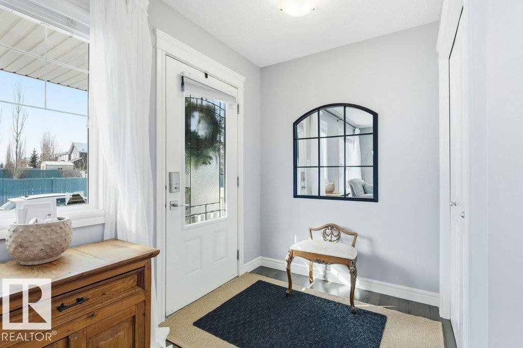 The entryway features a white front door with decorative glass, a window with sheer white curtains, and light gray walls - 16720 15 Avenue, Edmonton, AB - Indoor Photo Showing Other Room