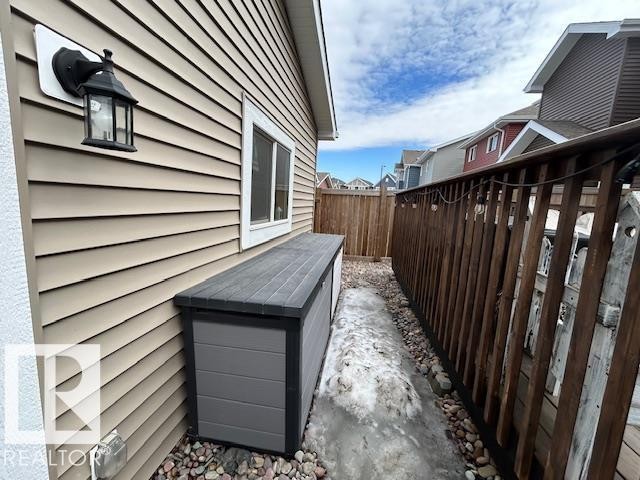 The exterior features tan horizontal siding, a white-framed window, and a black wall lantern - 16720 15 Avenue, Edmonton, AB - Outdoor With Exterior