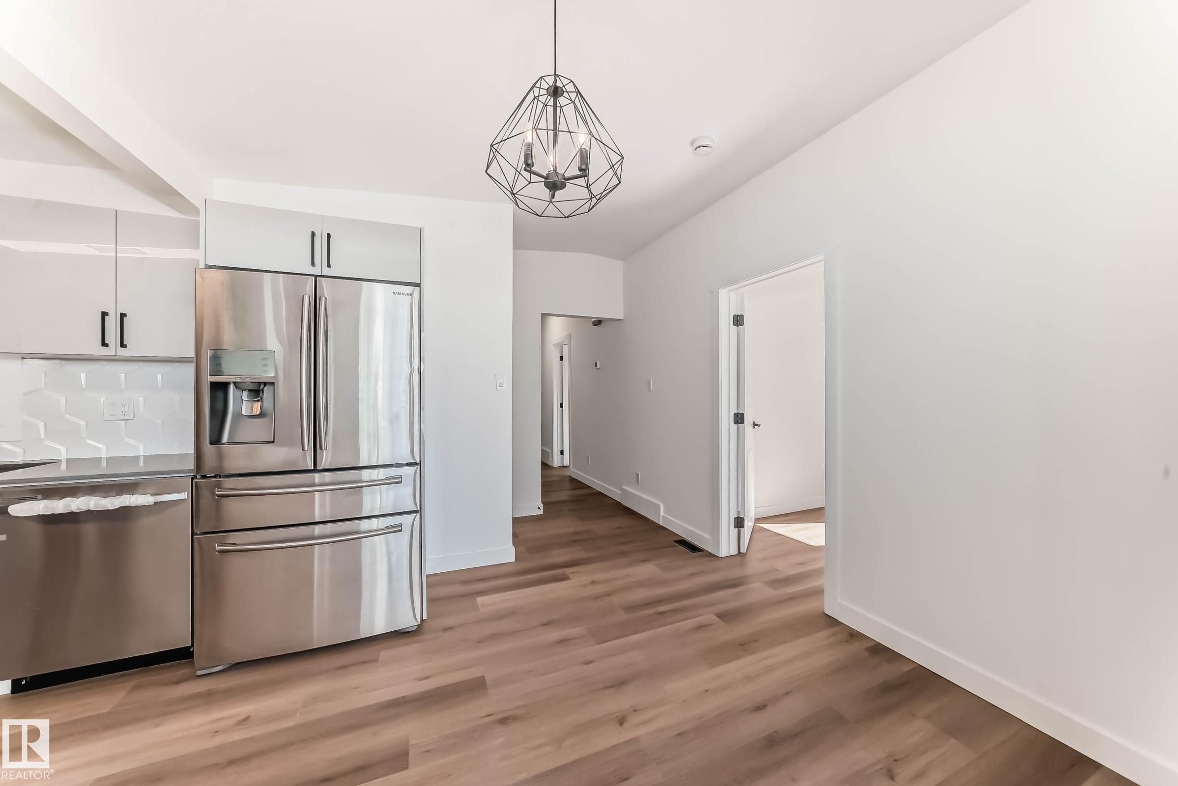 The kitchen features stainless steel appliances, including a refrigerator and dishwasher, light-colored cabinetry, and a hexagon tile backsplash - 7220 152A Ave, Edmonton, AB - Indoor Photo Showing Kitchen