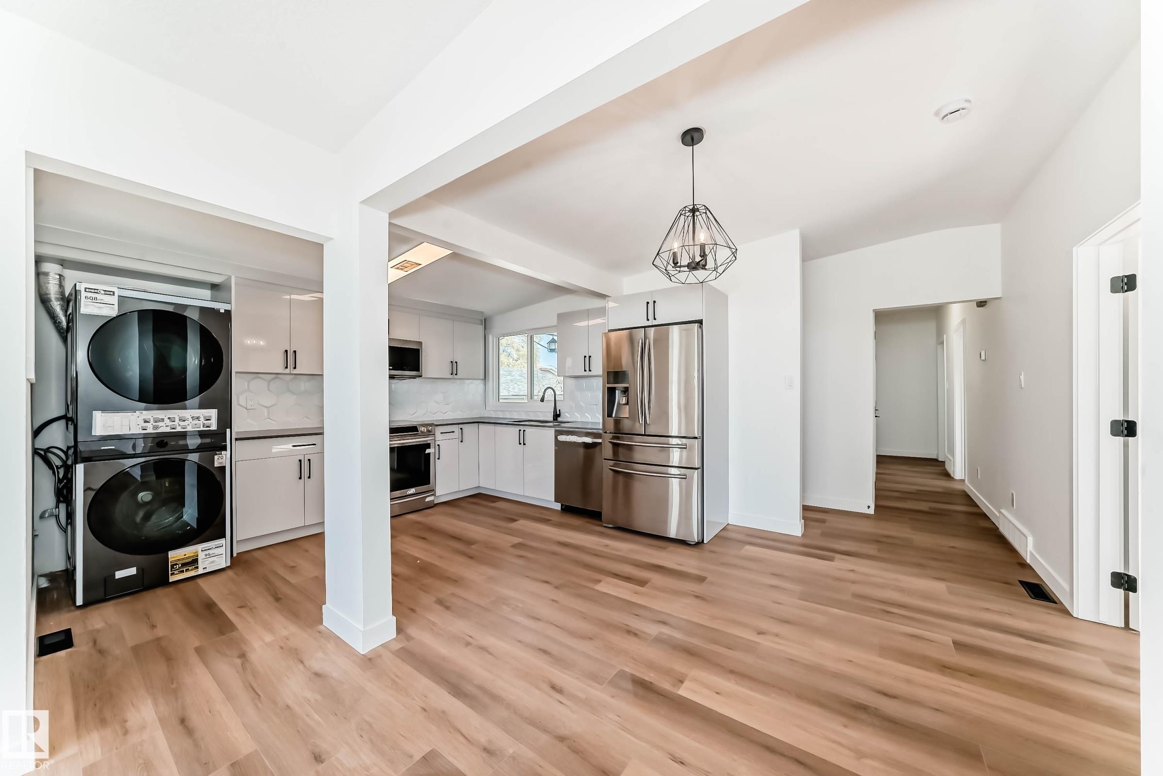Open concept kitchen featuring stainless steel appliances, light wood flooring, contemporary light fixtures, and white cabinetry - 7220 152A Ave, Edmonton, AB - Indoor Photo Showing Kitchen